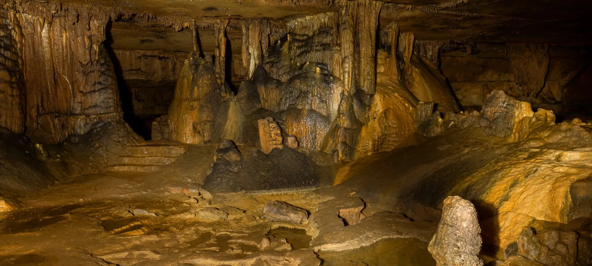 Dimly lit cave interior with stalactites and stalagmites.