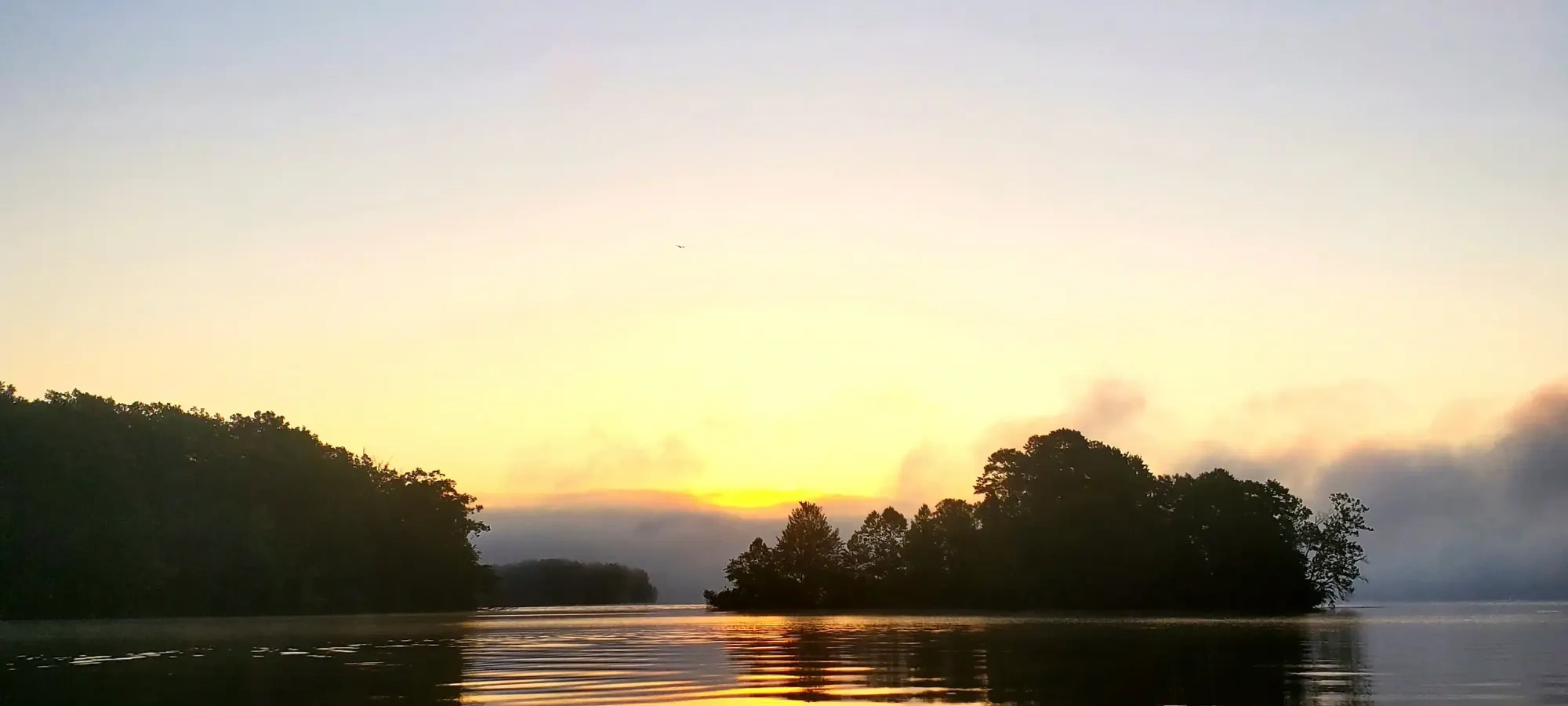 Sunrise over a calm lake with silhouetted trees and reflected colors.