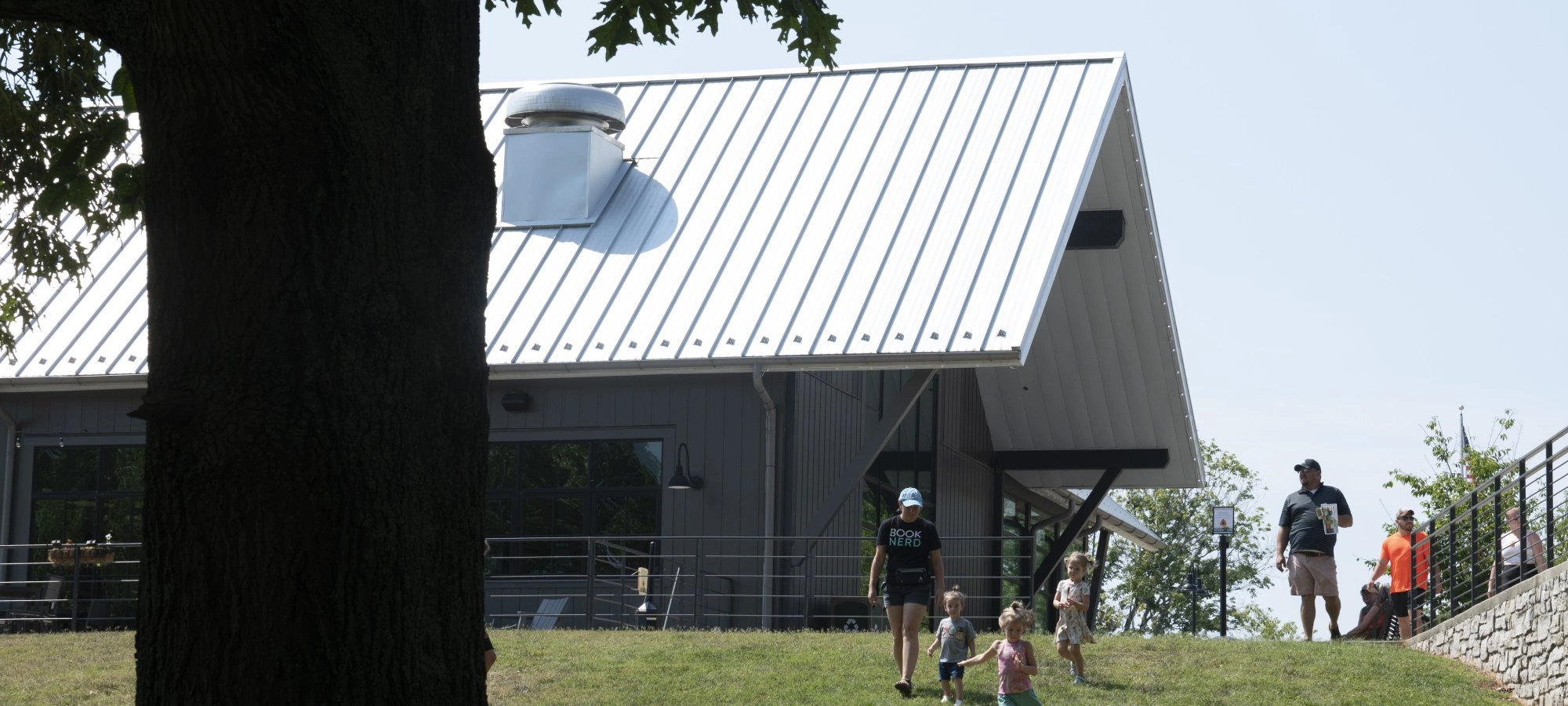 Children and adults walking on a grassy hill near a modern gray lodge building with a sloped metal roof.