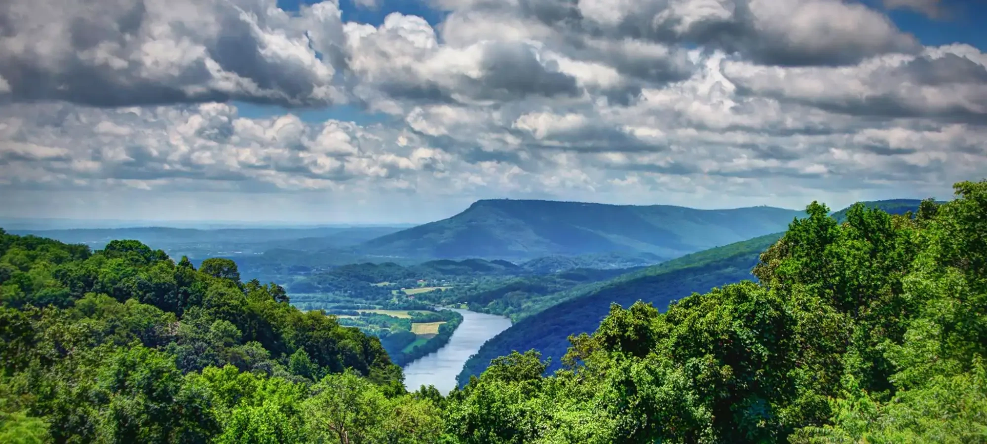 Lush green hills with a winding river under a cloudy sky.