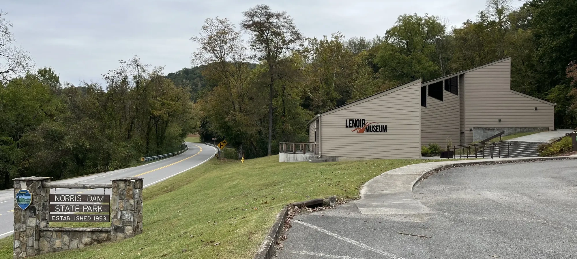 Lenoir Museum near curving road, surrounded by trees, cloudy sky overhead.