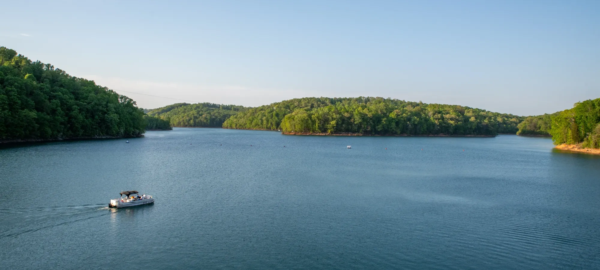 Boat on a serene lake surrounded by green hills under a clear blue sky.