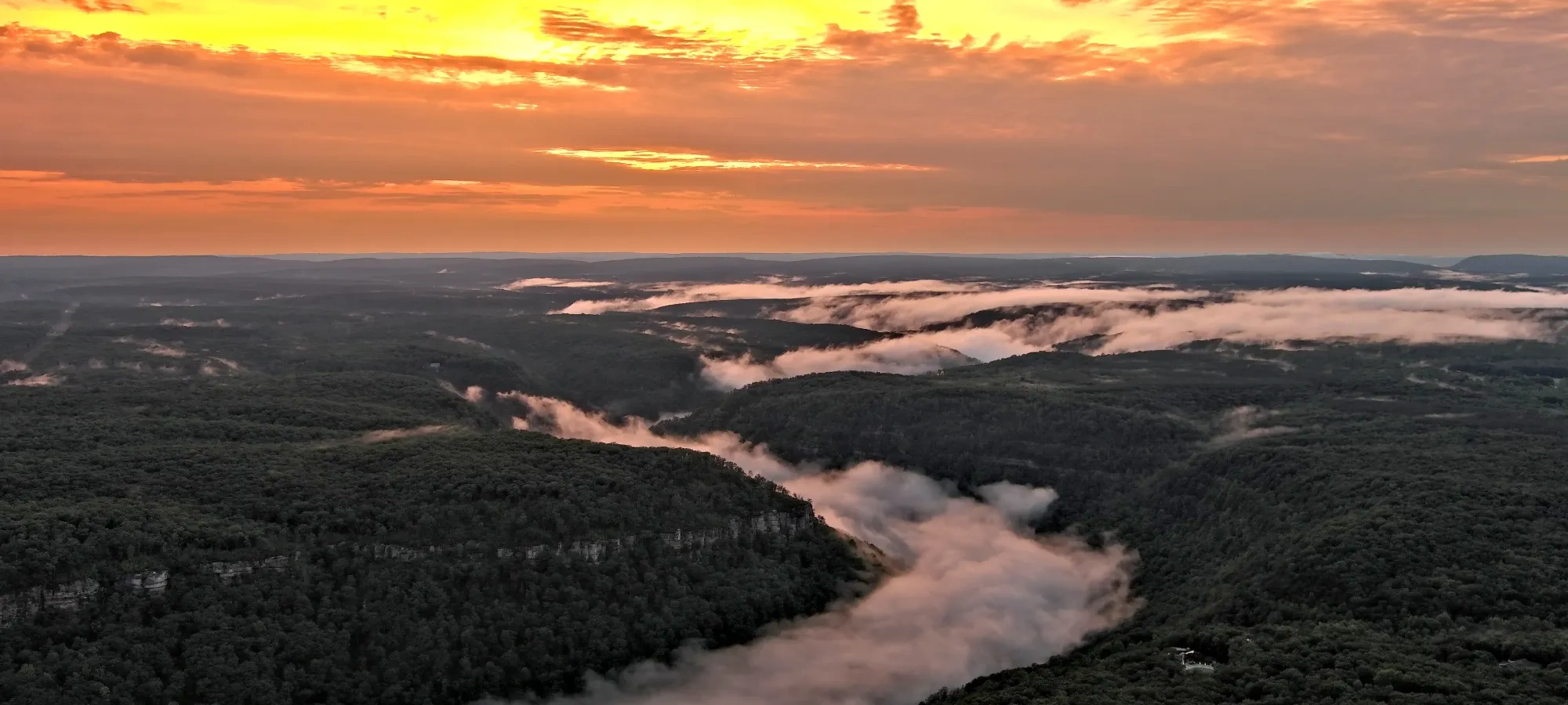Sunset over hills with clouds and mist in valleys.