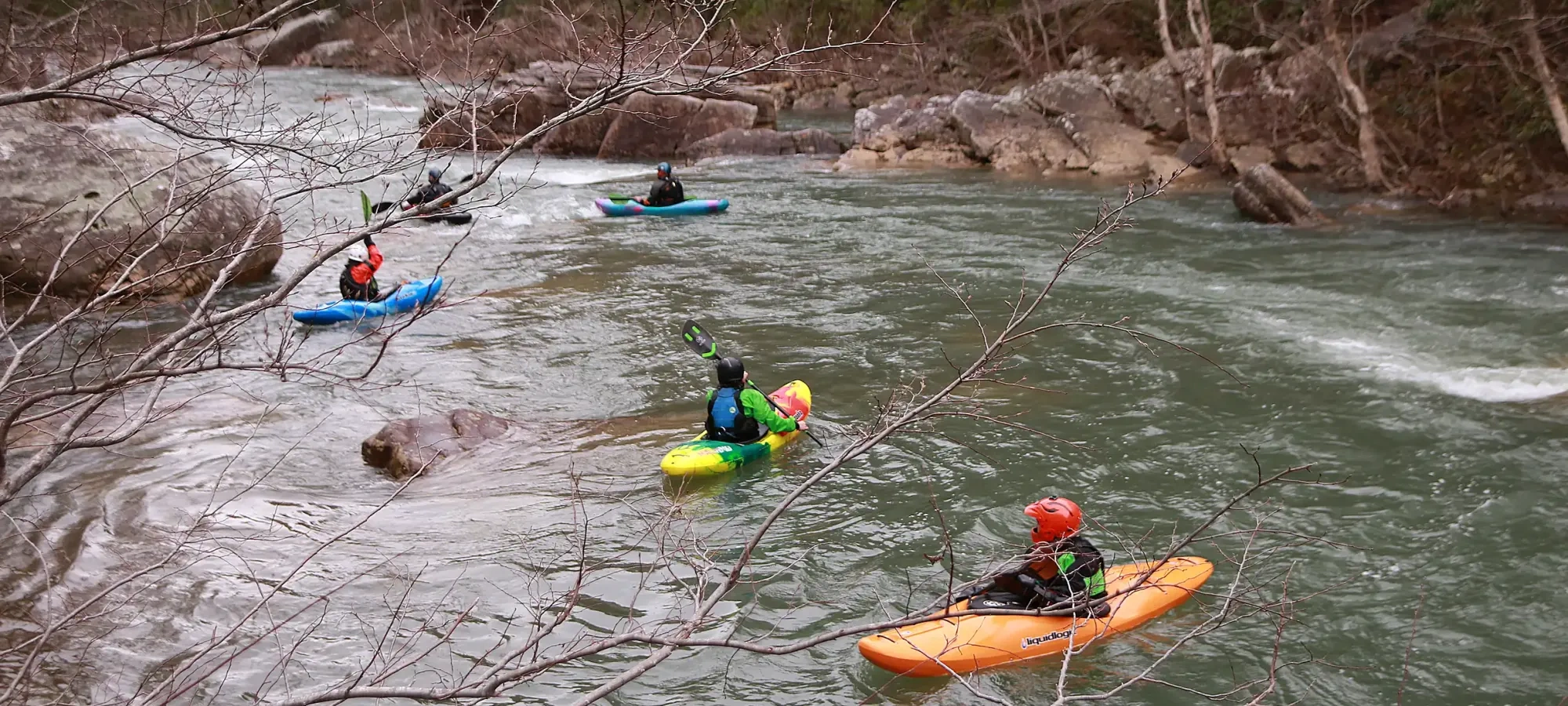 Kayakers paddling on a river surrounded by trees and rocks.