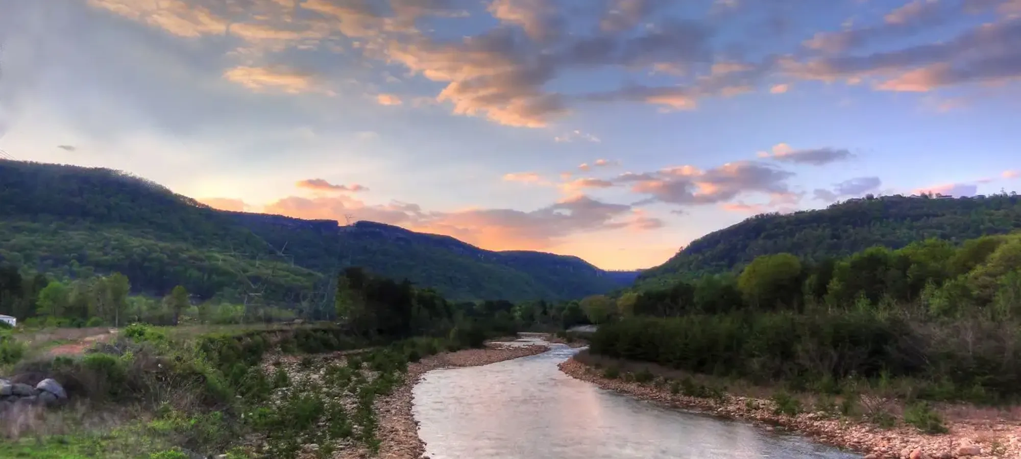 River winds through a lush valley at sunset, under colorful clouds.