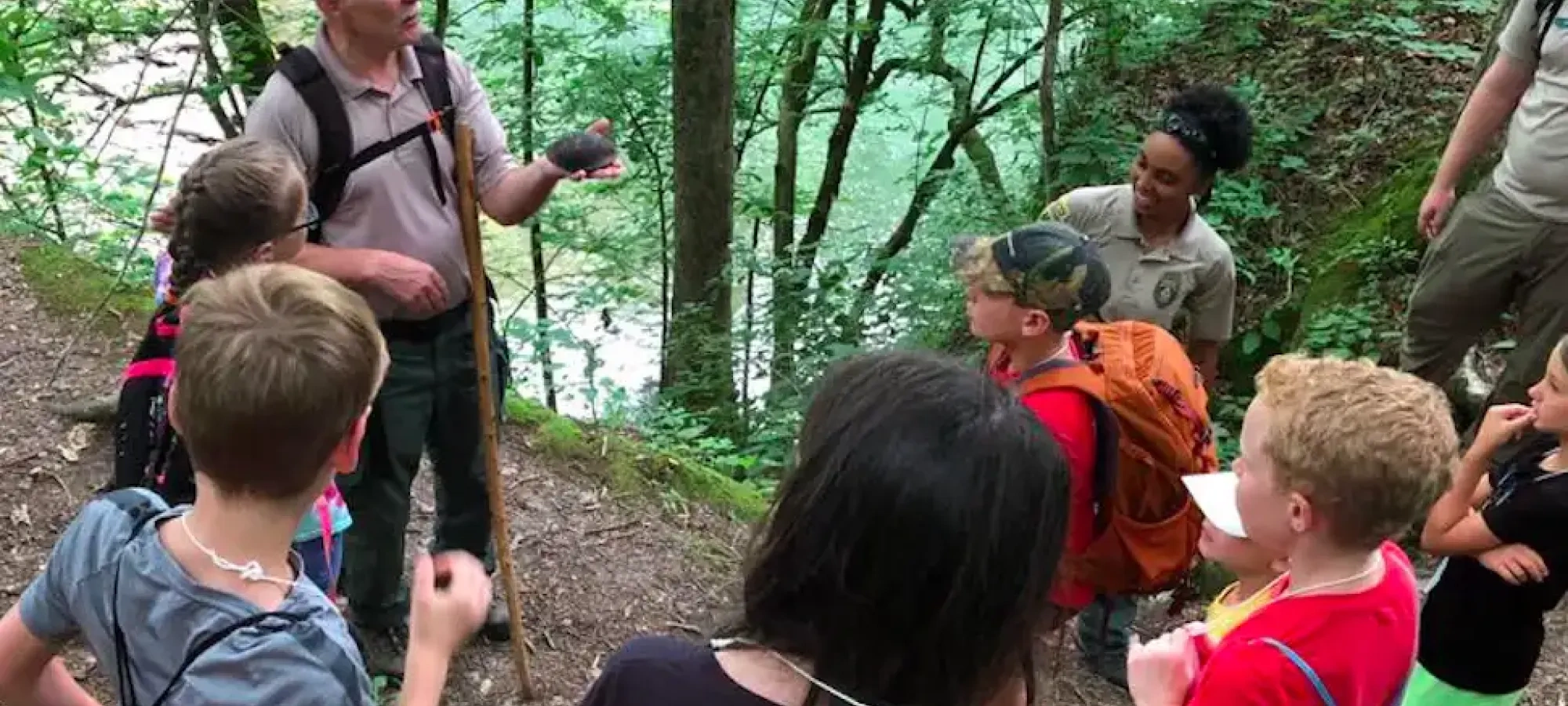 A guide showing a group of children a stone in a wooded area.