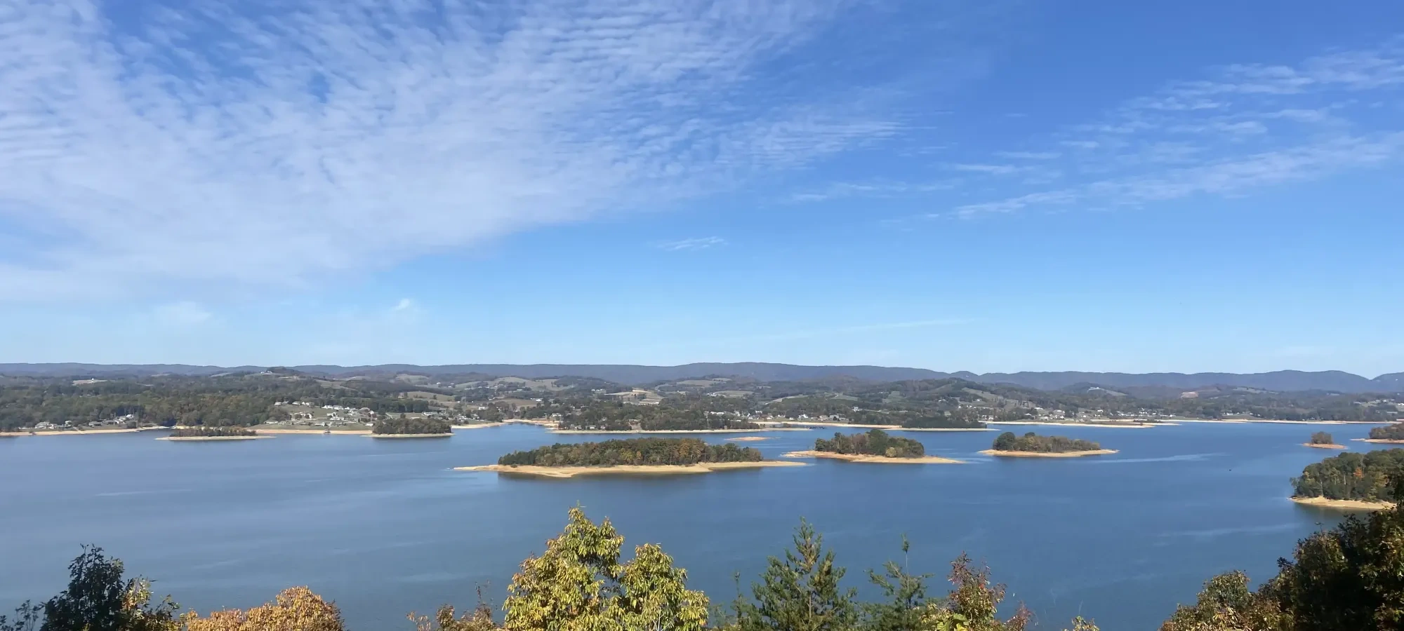 Blue lake with small islands, surrounded by distant hills and a clear, bright sky.
