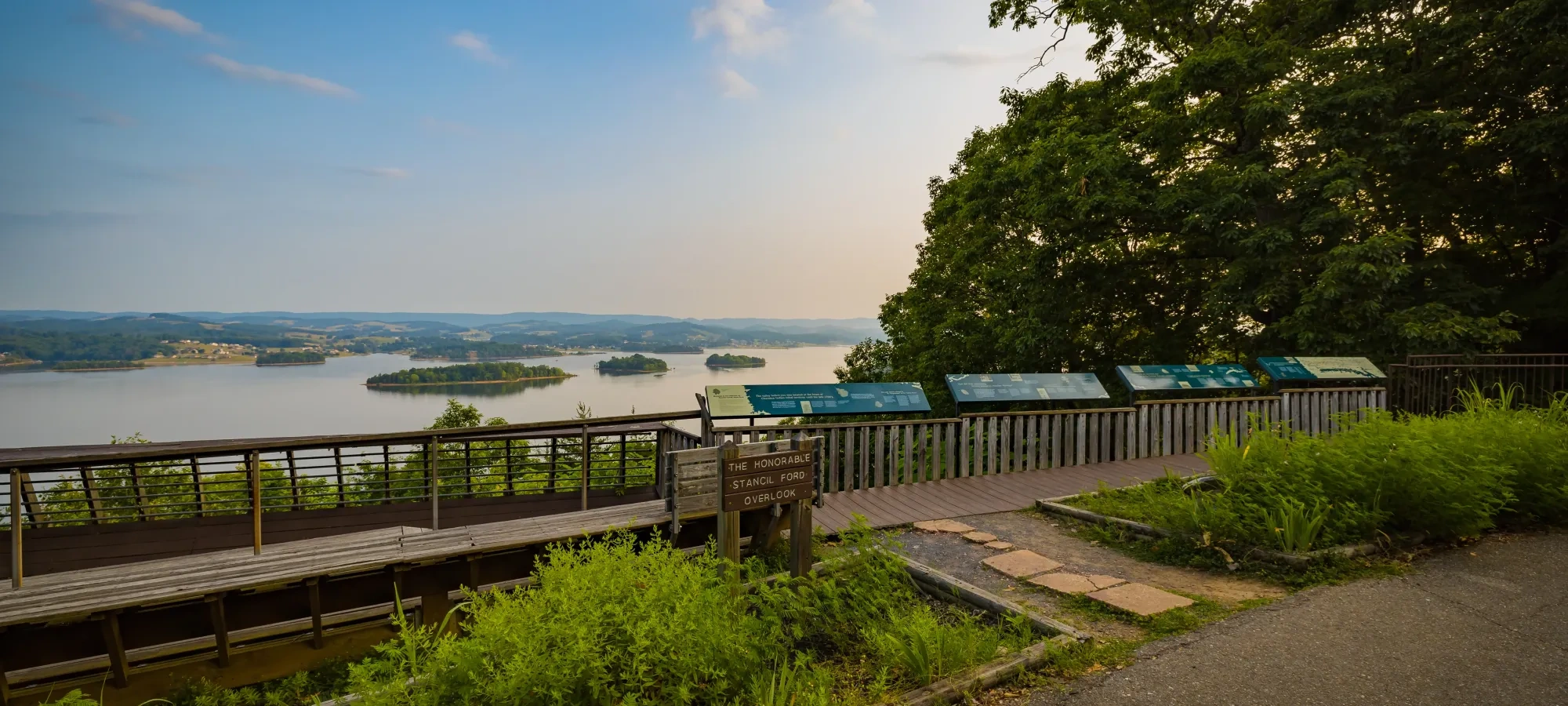 Scenic lake view from overlook deck with trees and informational signs.