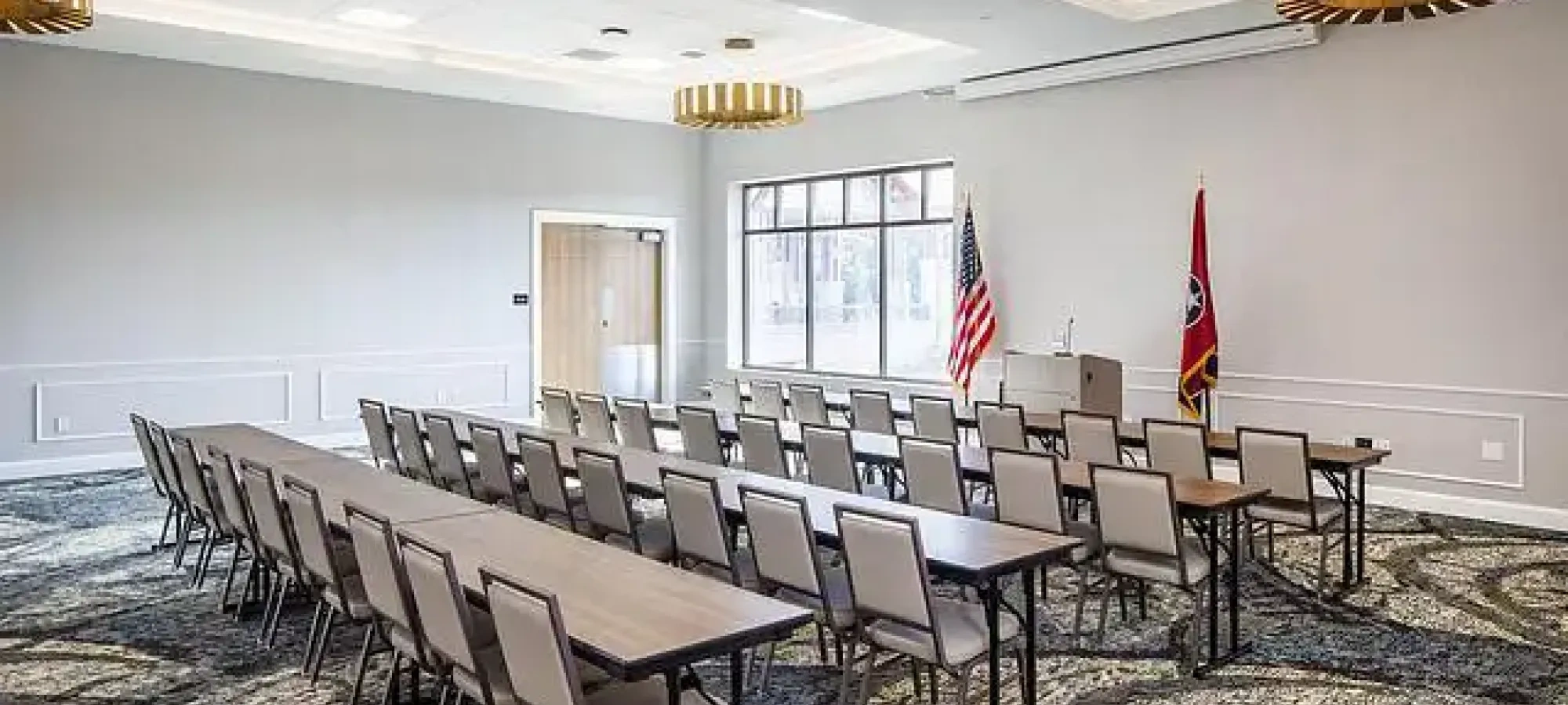 Conference room with arranged chairs, two flags, and elegant lighting.