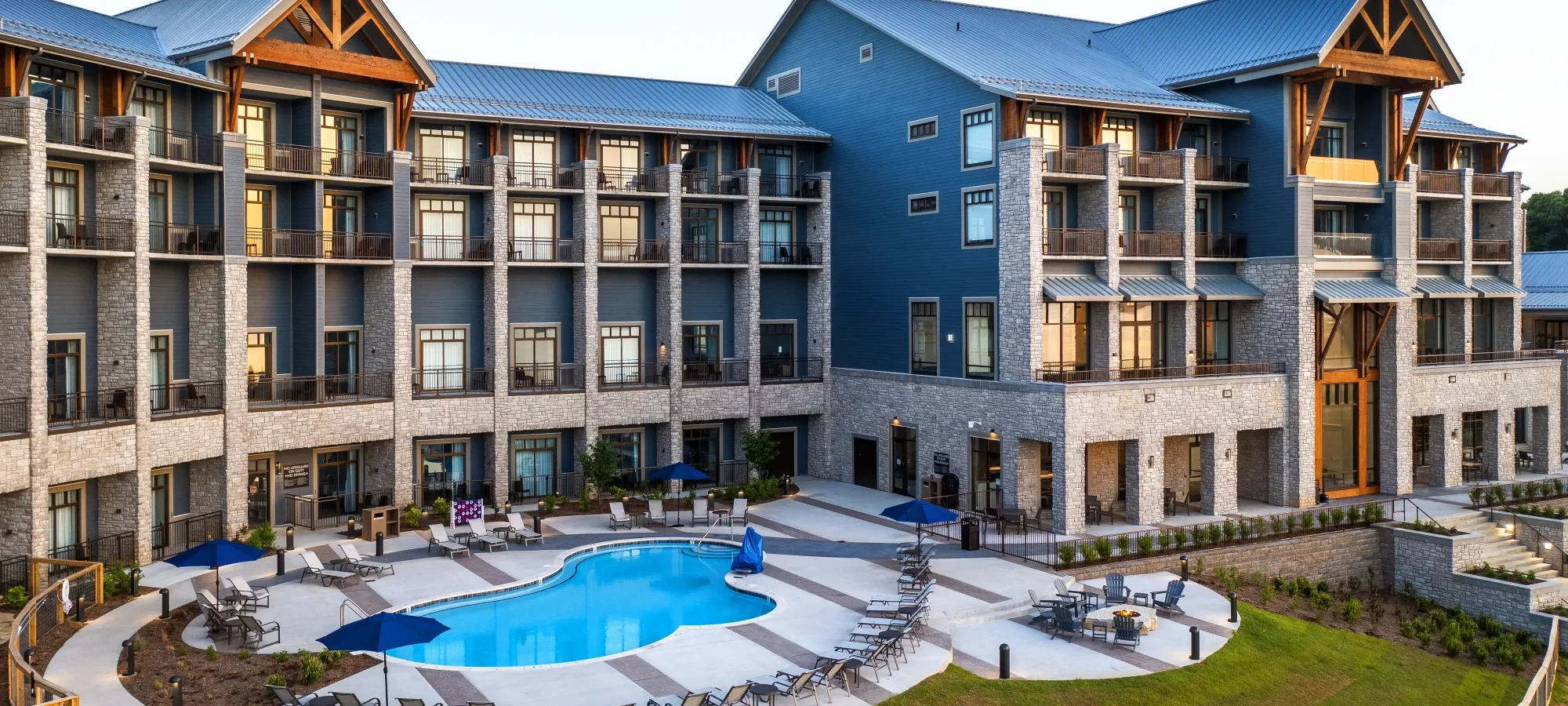 Hotel with balconies and a pool, surrounded by chairs and umbrellas.