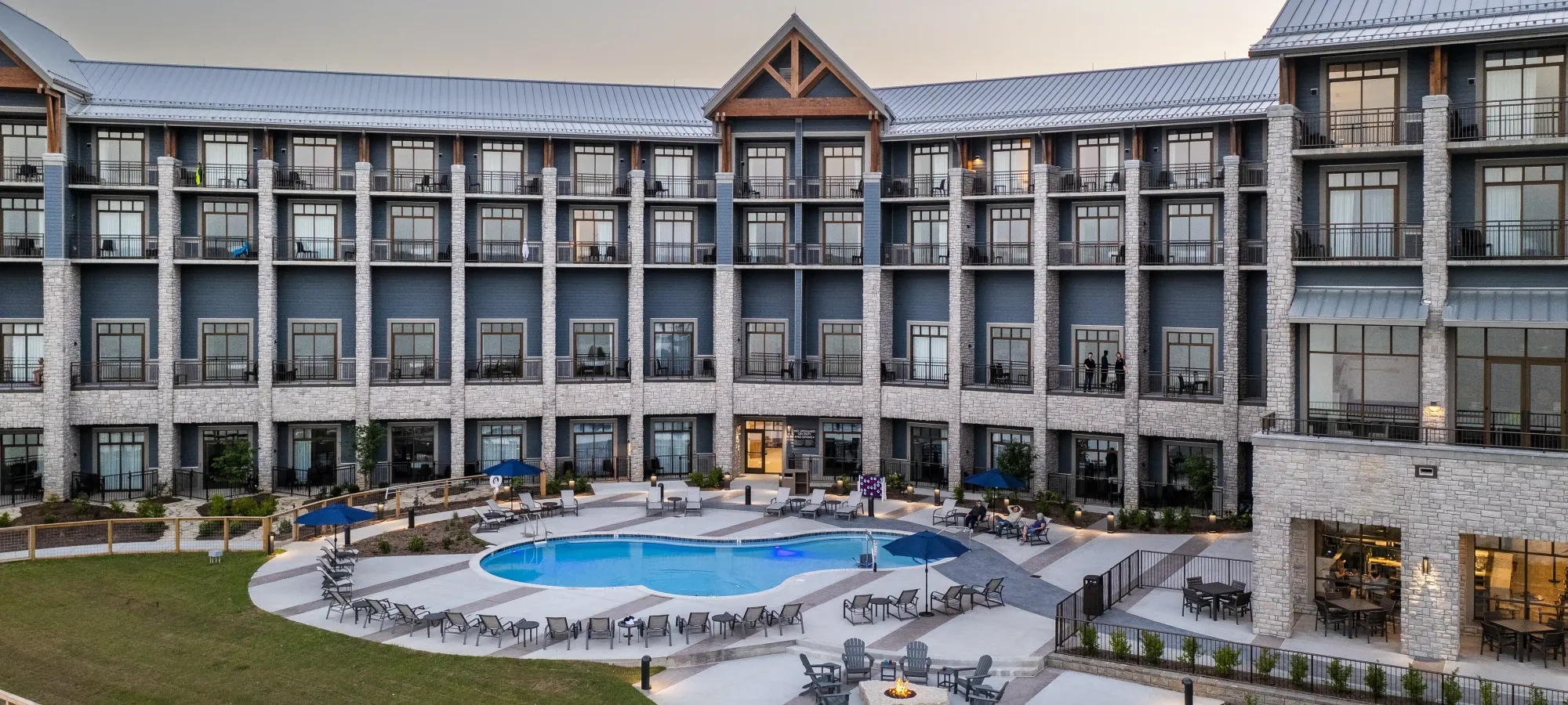 Hotel courtyard with pool, surrounded by lounge chairs and fire pit, under a clear sky.