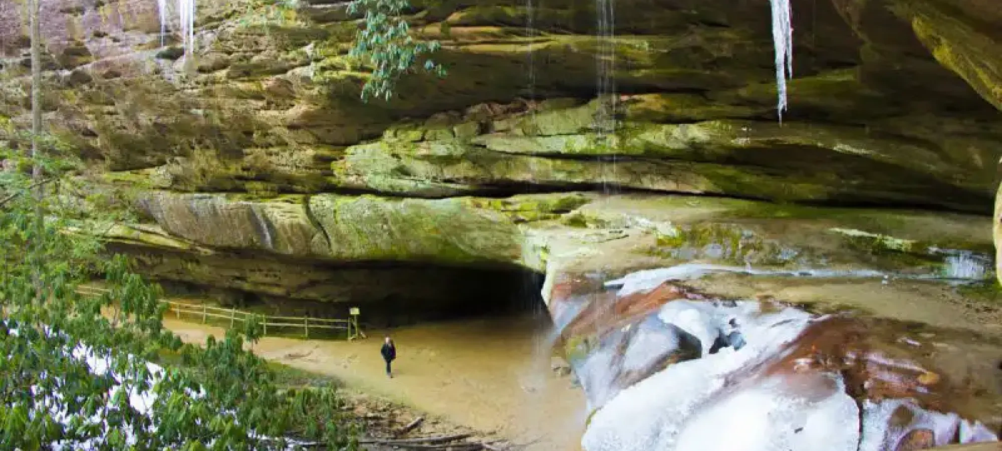Person exploring a moss-covered cave with icicles and a frozen waterfall.