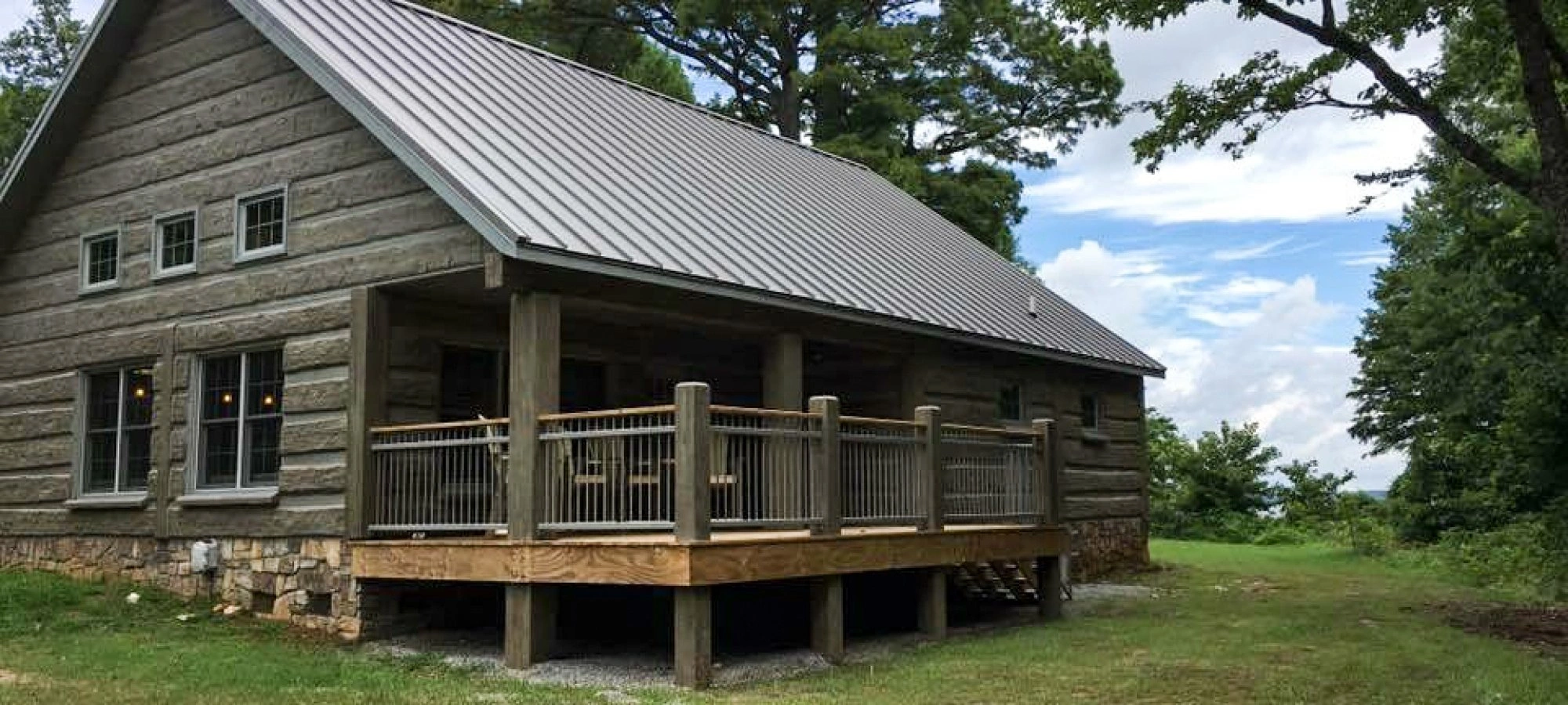 Rustic log cabin with a metal roof, surrounded by trees and grass.
