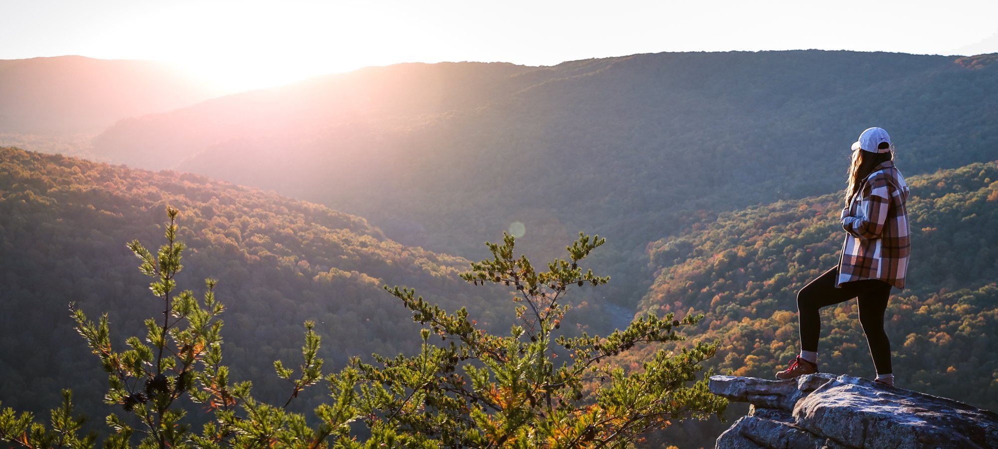 Women standing on rock that's over a valley looking at the sunset