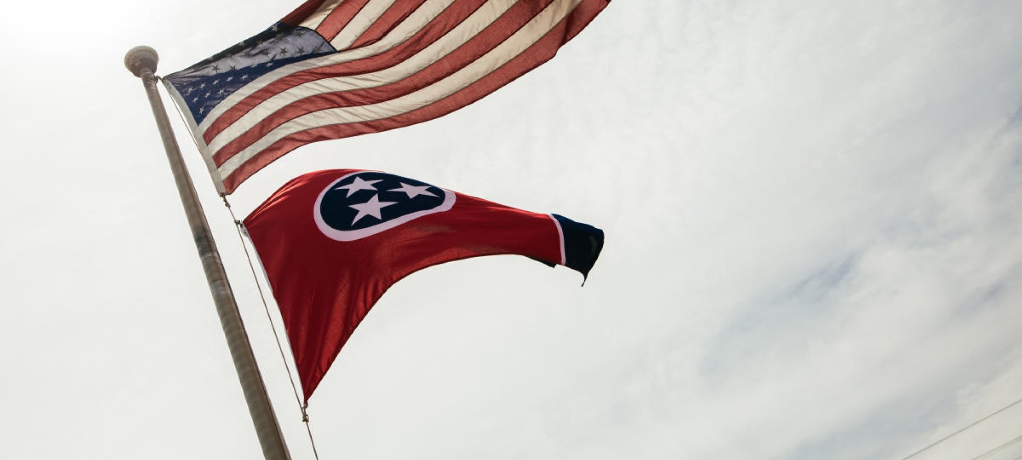 American and tennessee flags blowing in wind on a pole