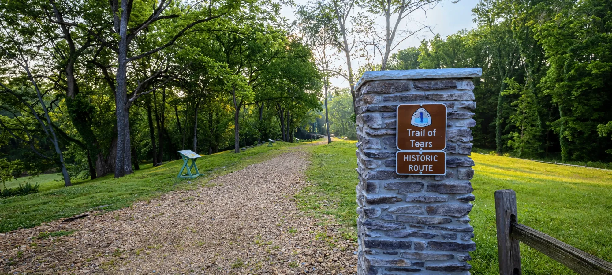 Trail lined with trees and a stone sign reading 