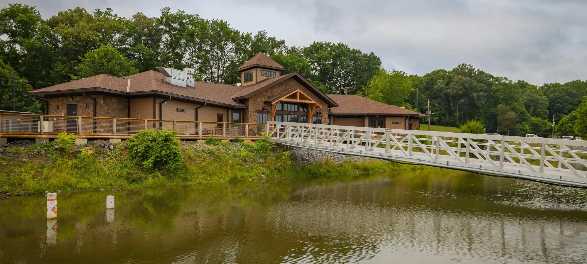 Lakeside building with wooden bridge and surrounding greenery.