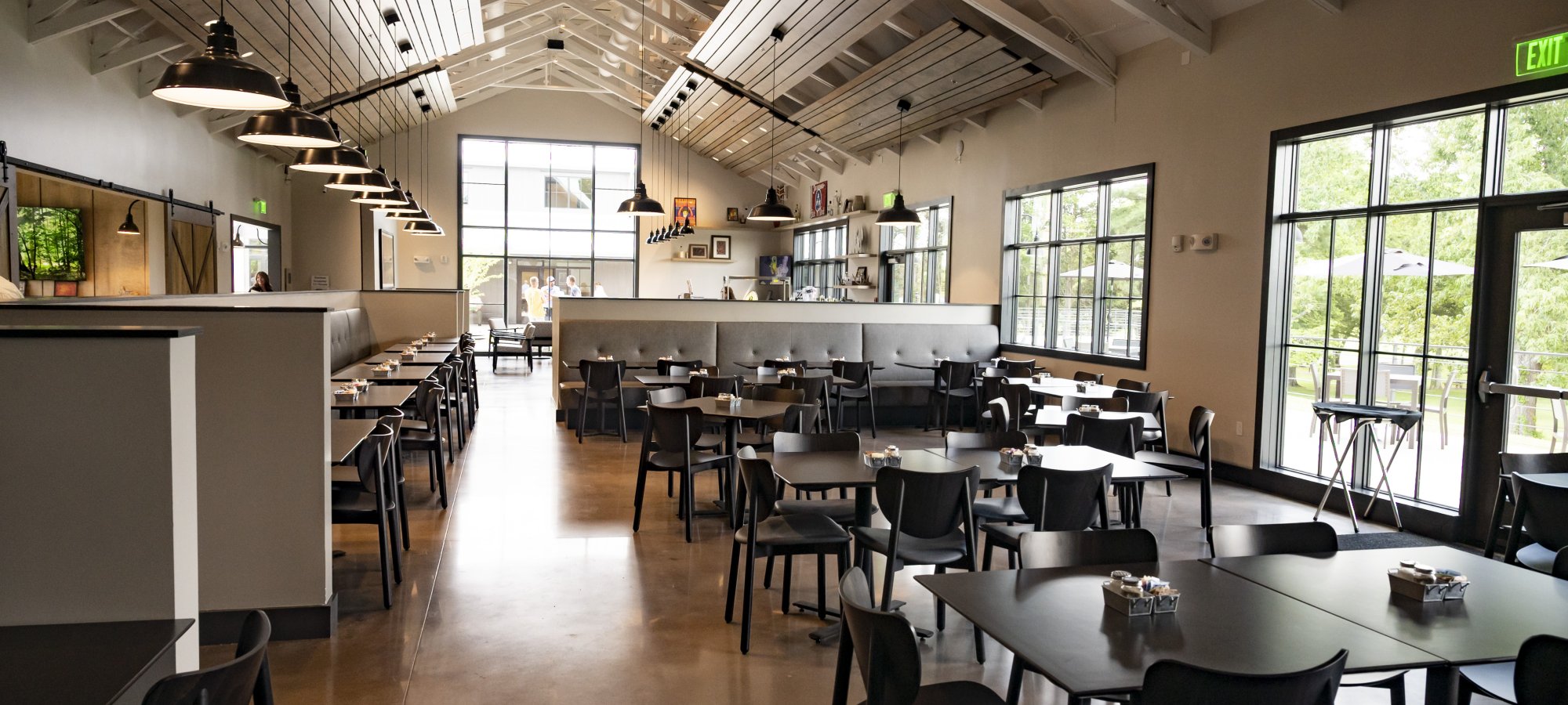 Spacious restaurant interior with high ceilings, modern black tables, and chairs. Large windows let in natural light, creating a calm, inviting atmosphere.