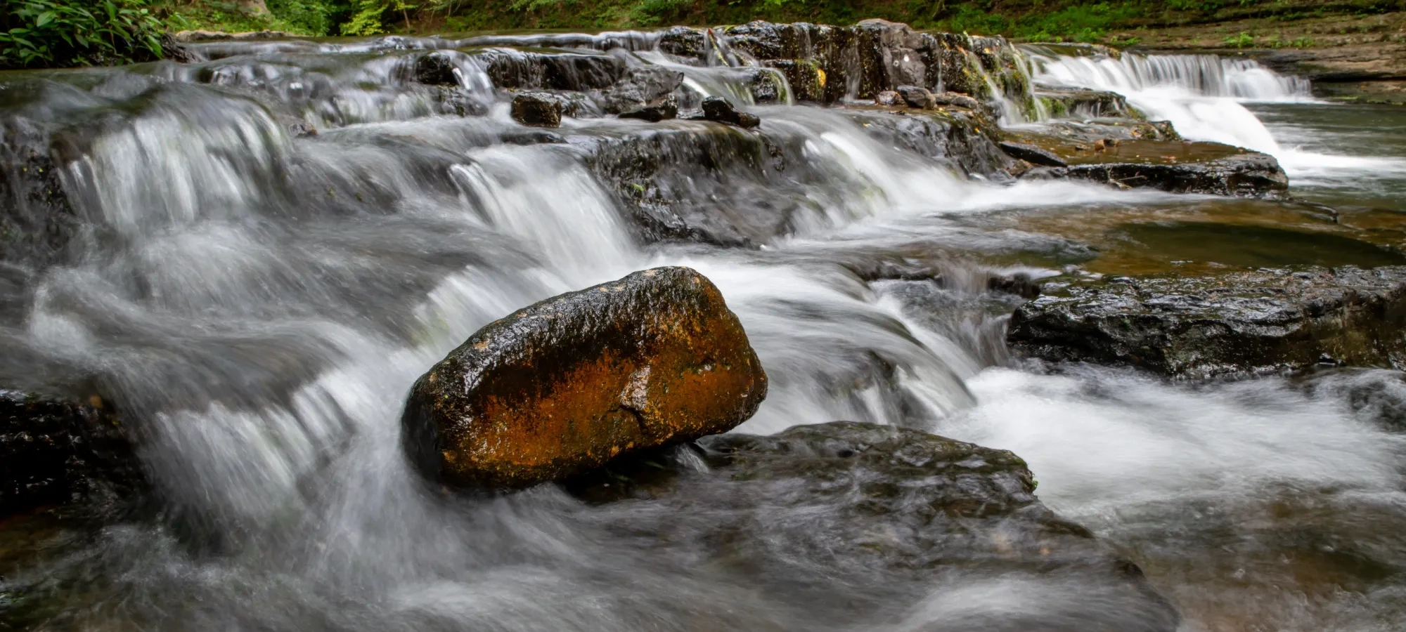 Flowing waterfall over rocks with lush green forest in the background.