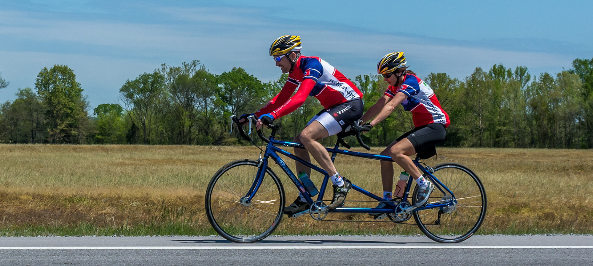 Two cyclists on a tandem bike ride along a rural road.