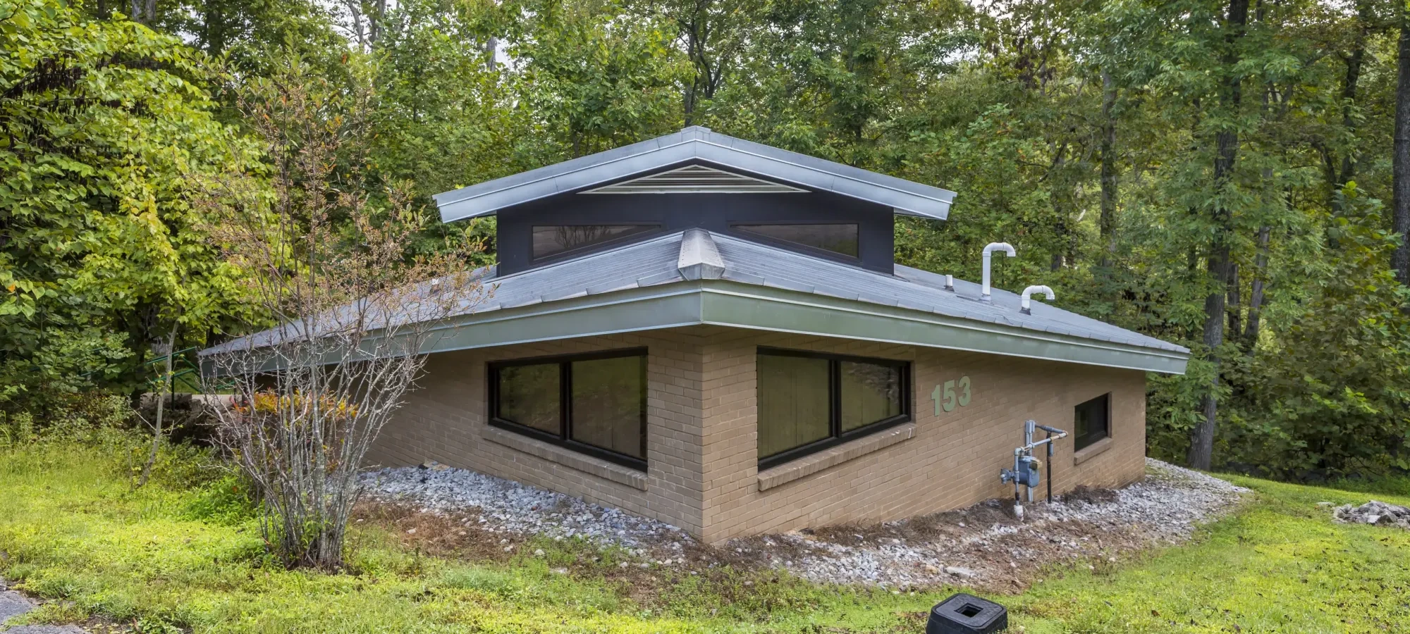 Mid-century modern house with a sloped roof, surrounded by trees.