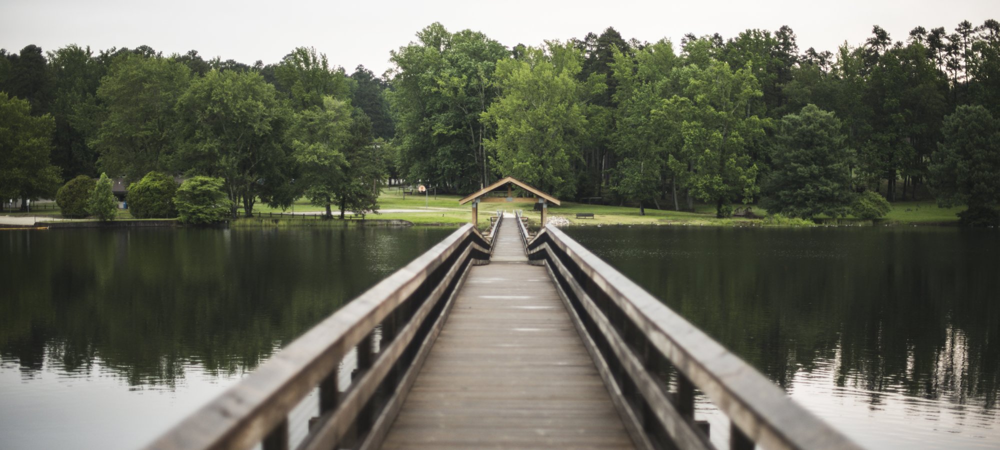 wooden bridge extending across a lake with guard rails.