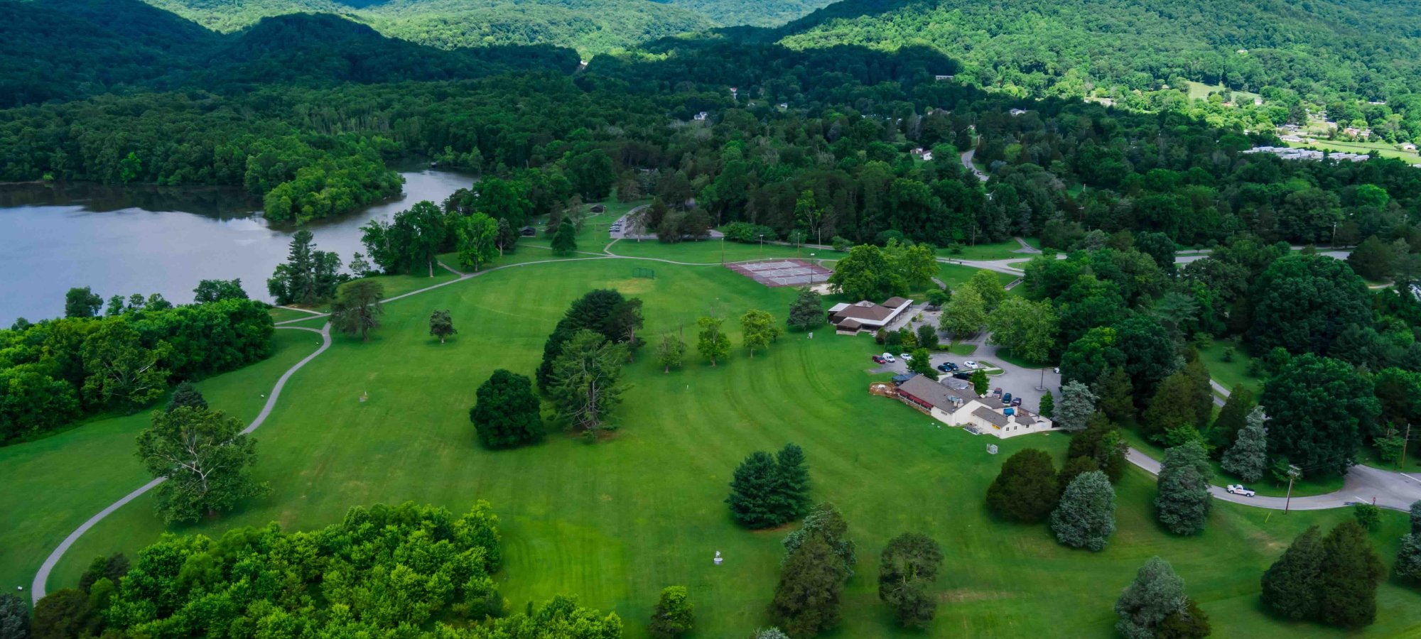 arial view of park and can see the parks trail, lake, buildings, trees, and mountains