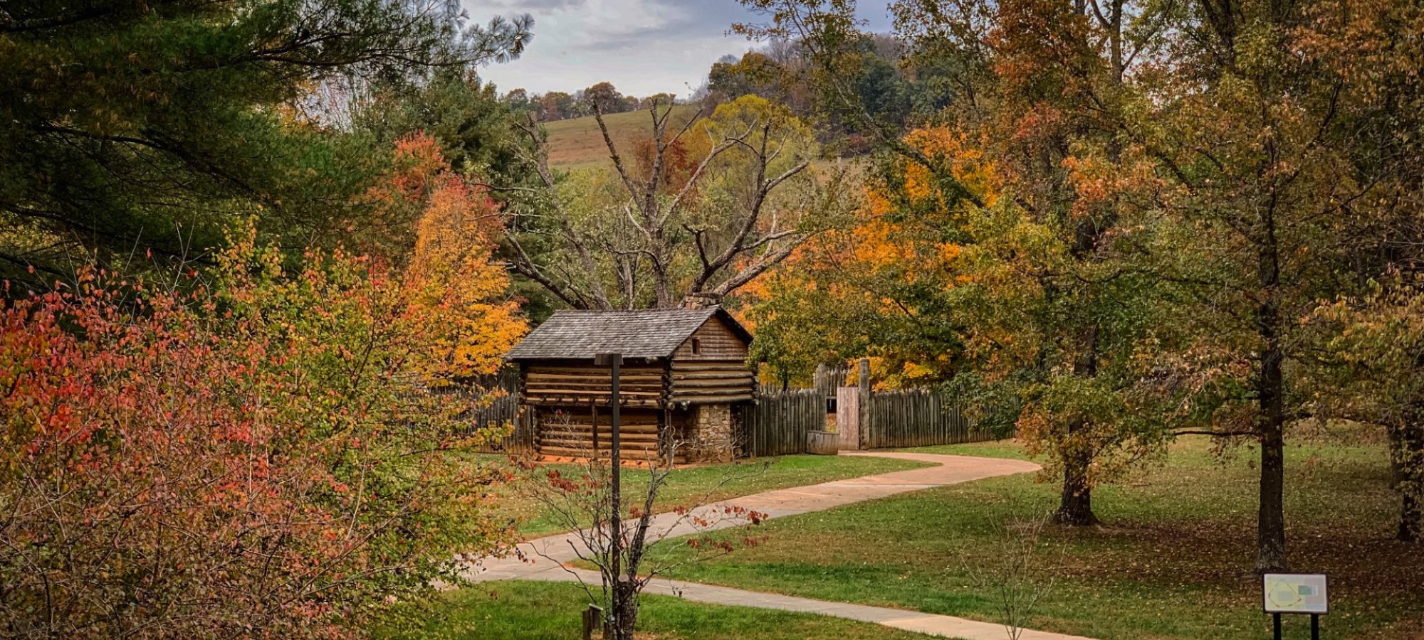autumn colorful trees with paths leading to a historic log cabin building 