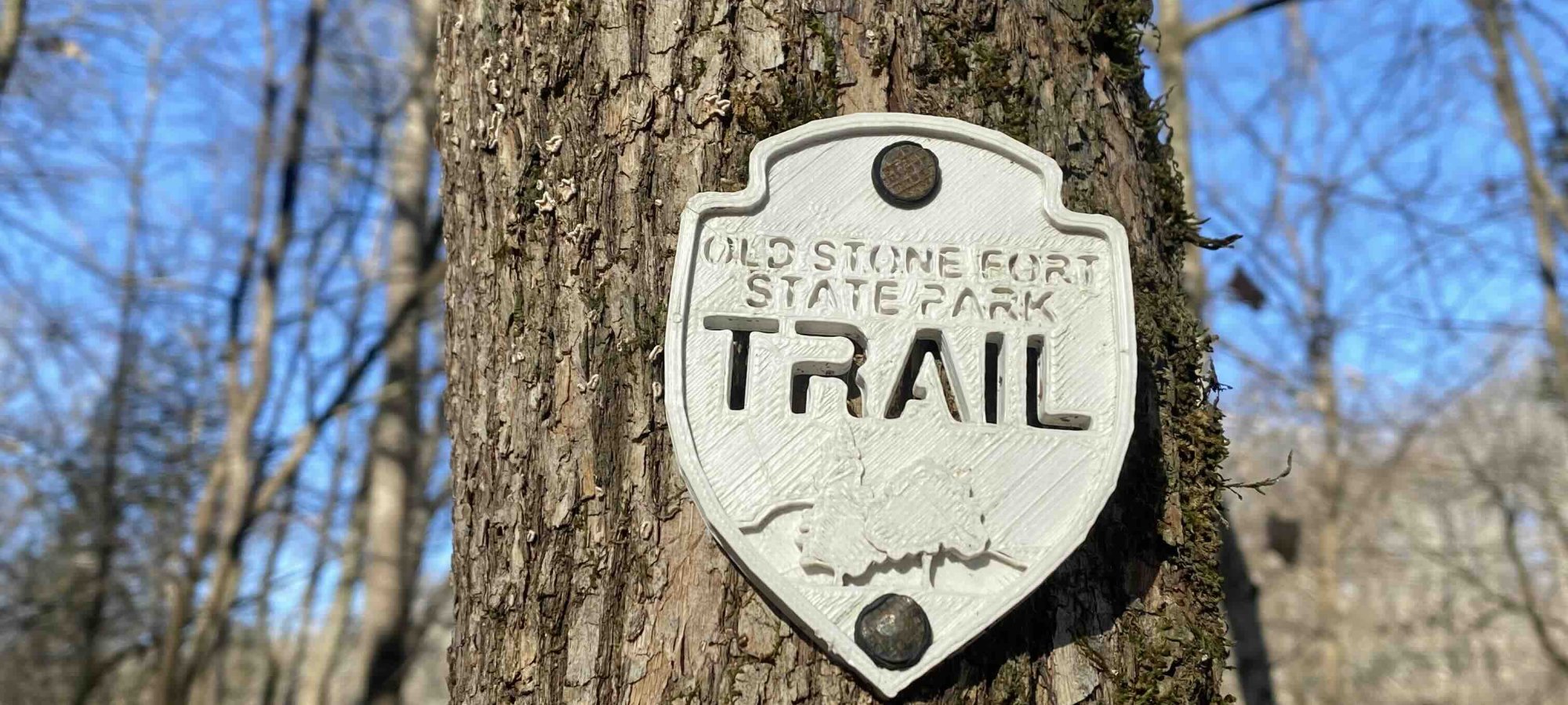 sign placed on a tree that says old stone fort state park trail