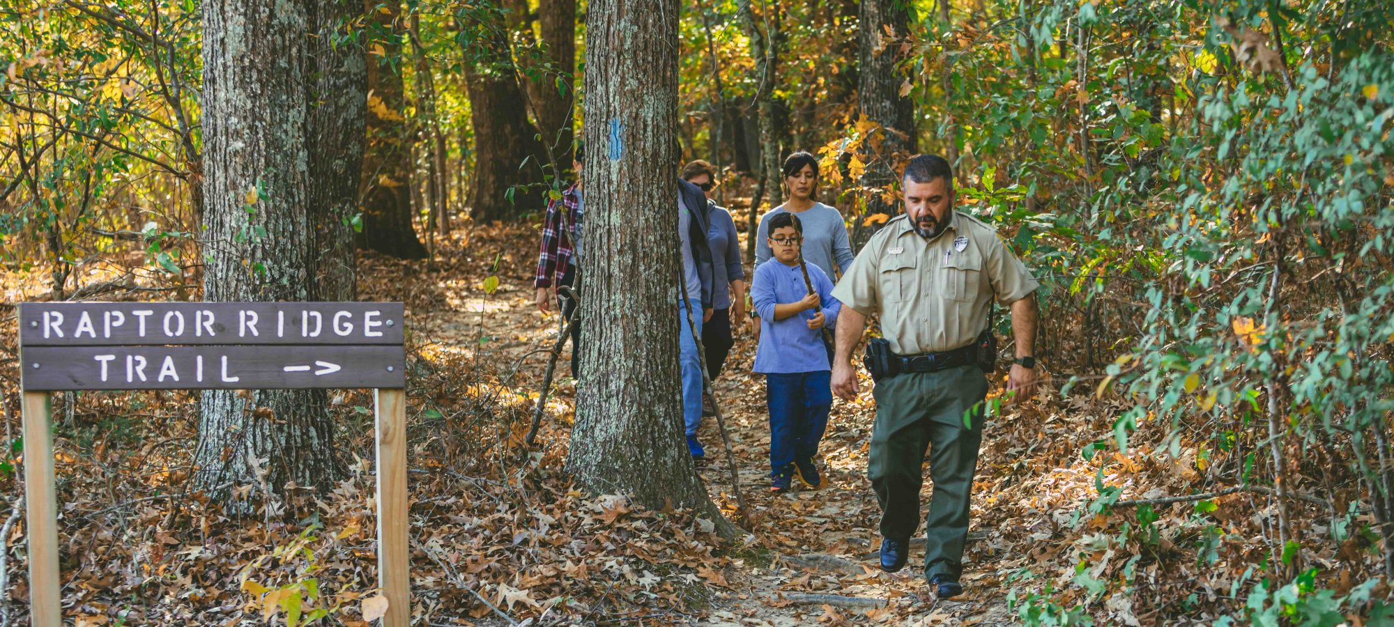 group of people with a ranger going on a trail with a wooden sign that says raptor trail