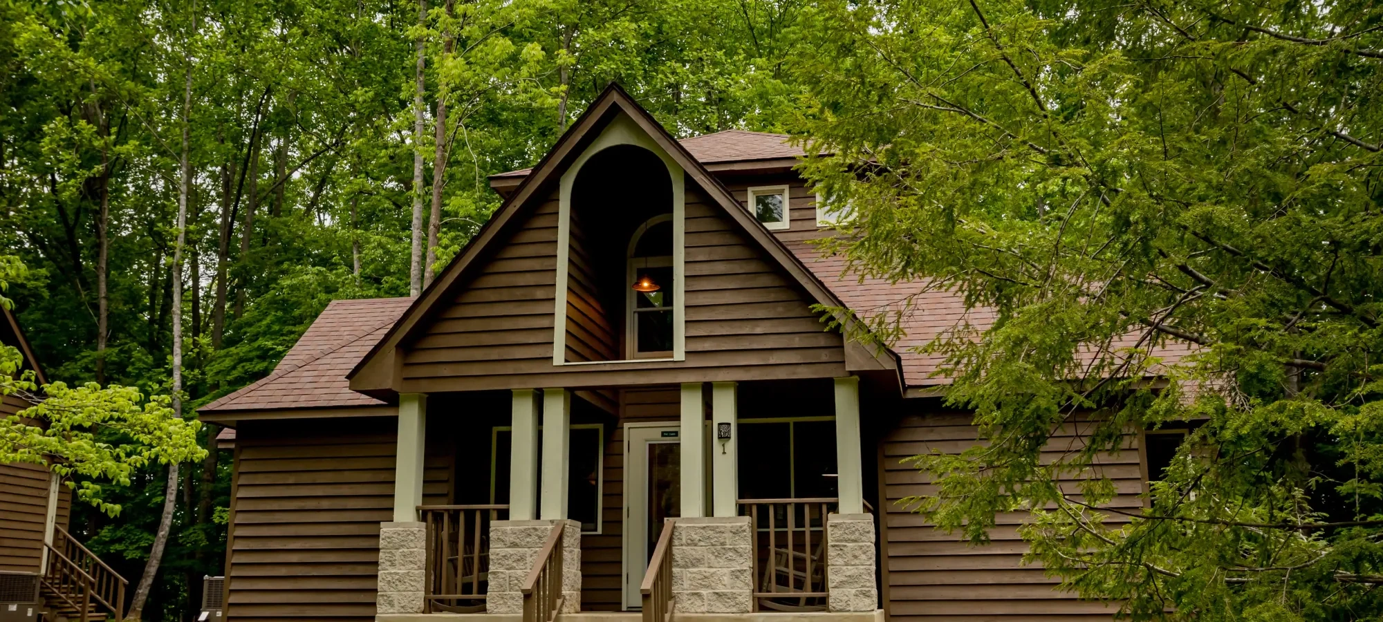 Brown cabin surrounded by green trees, pathway with a lantern in front.