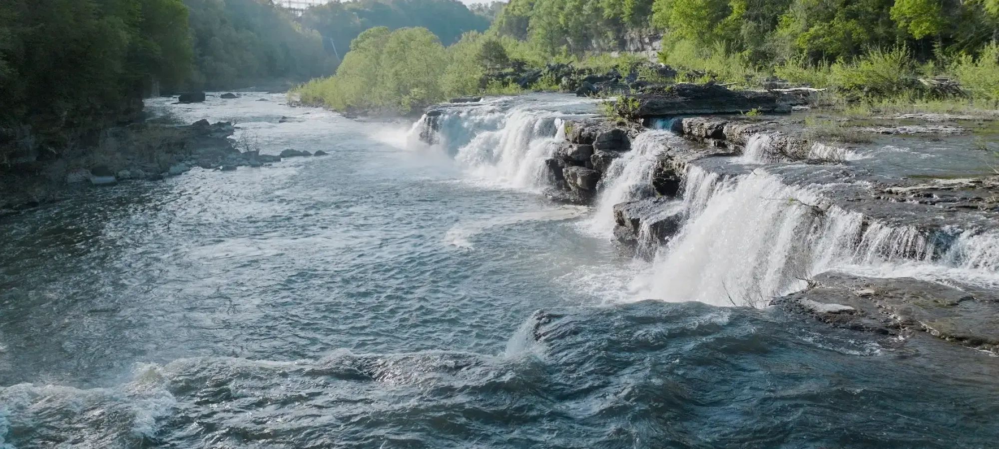 Waterfall cascading over rocks surrounded by green trees.