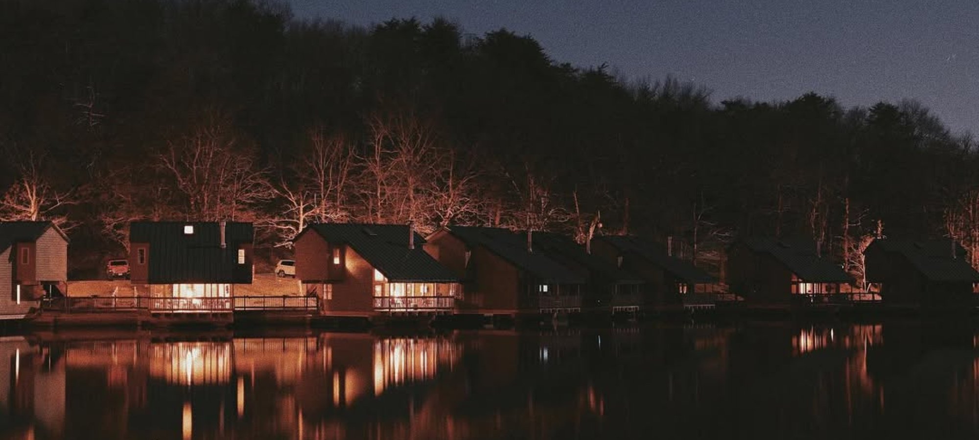 evening lighting with cabins on the shore. The lit up cabins reflect on the still lake water