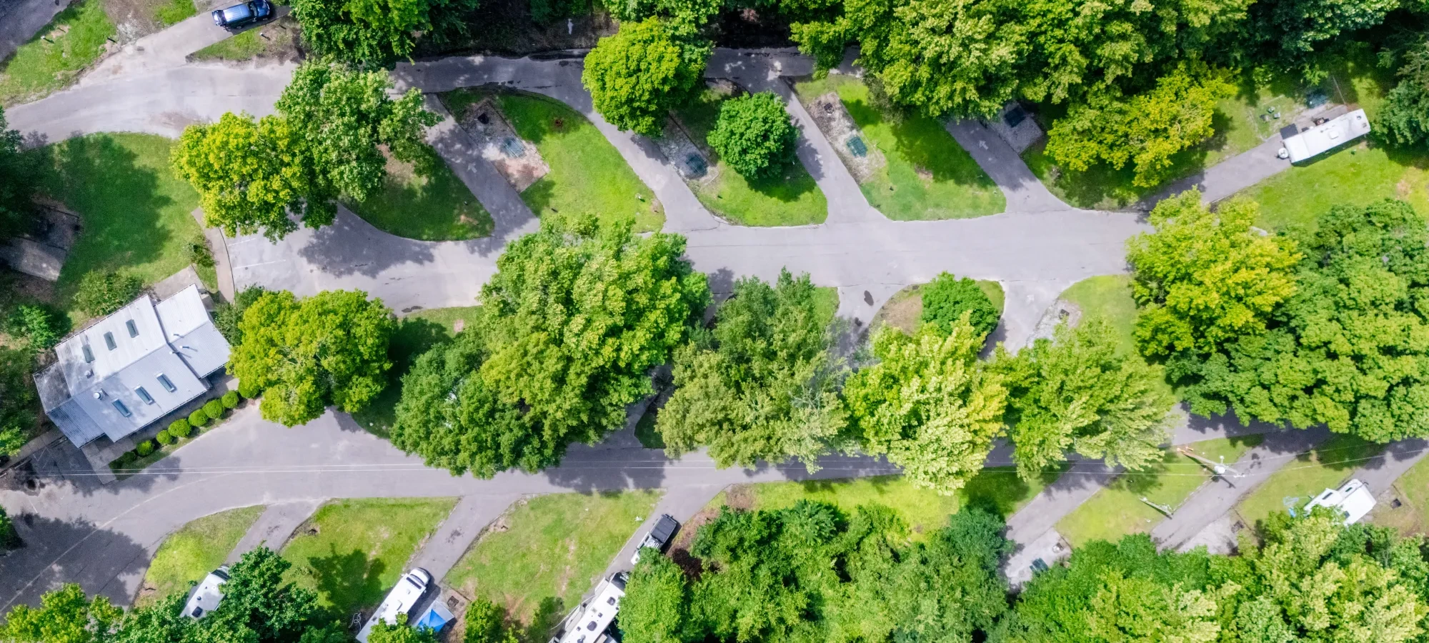 Aerial view of wooded RV park with roads and scattered parked trailers.