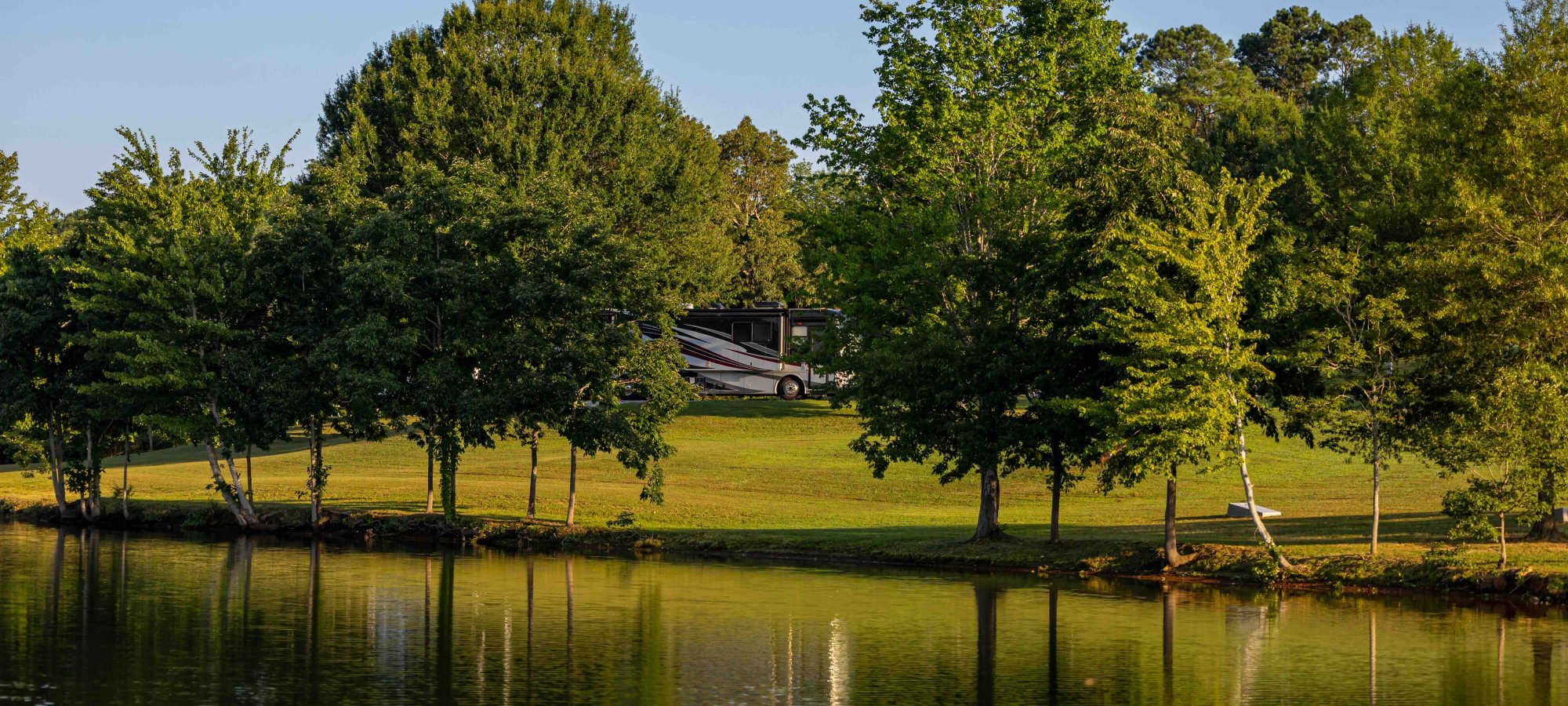 view of lake and across the water is land with some trees and an RV parked