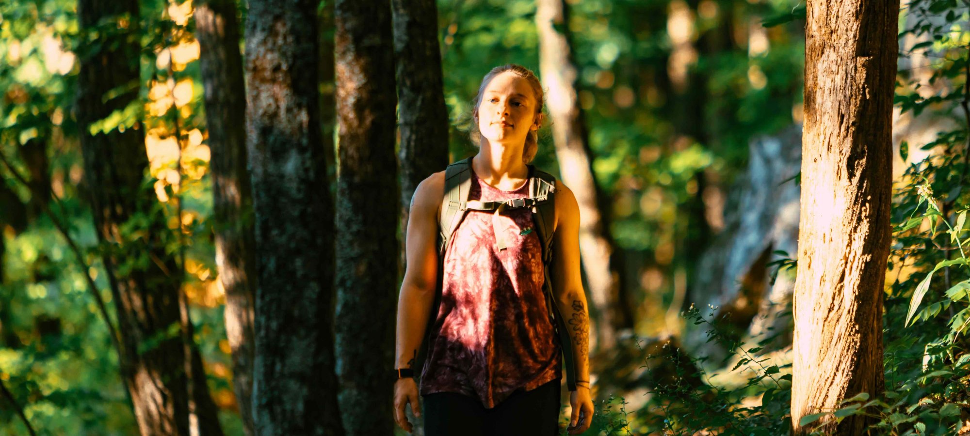 girl hiking in forest wearing a backpack and sun shining on her