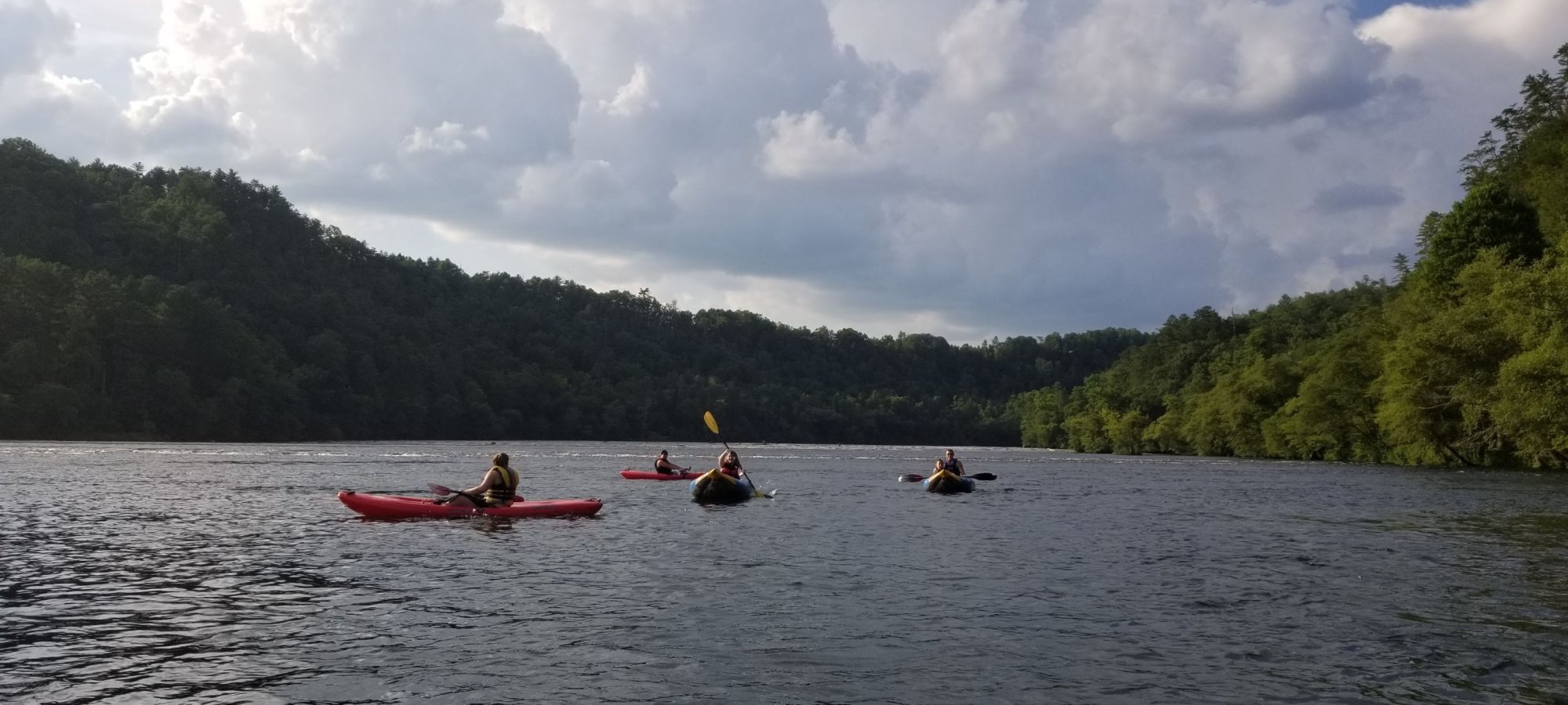 group of people far away paddling on a lake with mountains in the distance covered in trees