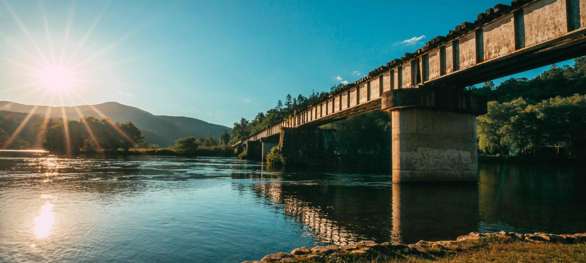 view of under a bridge during a sunset with water reflecting the sun and a mountain in the distance
