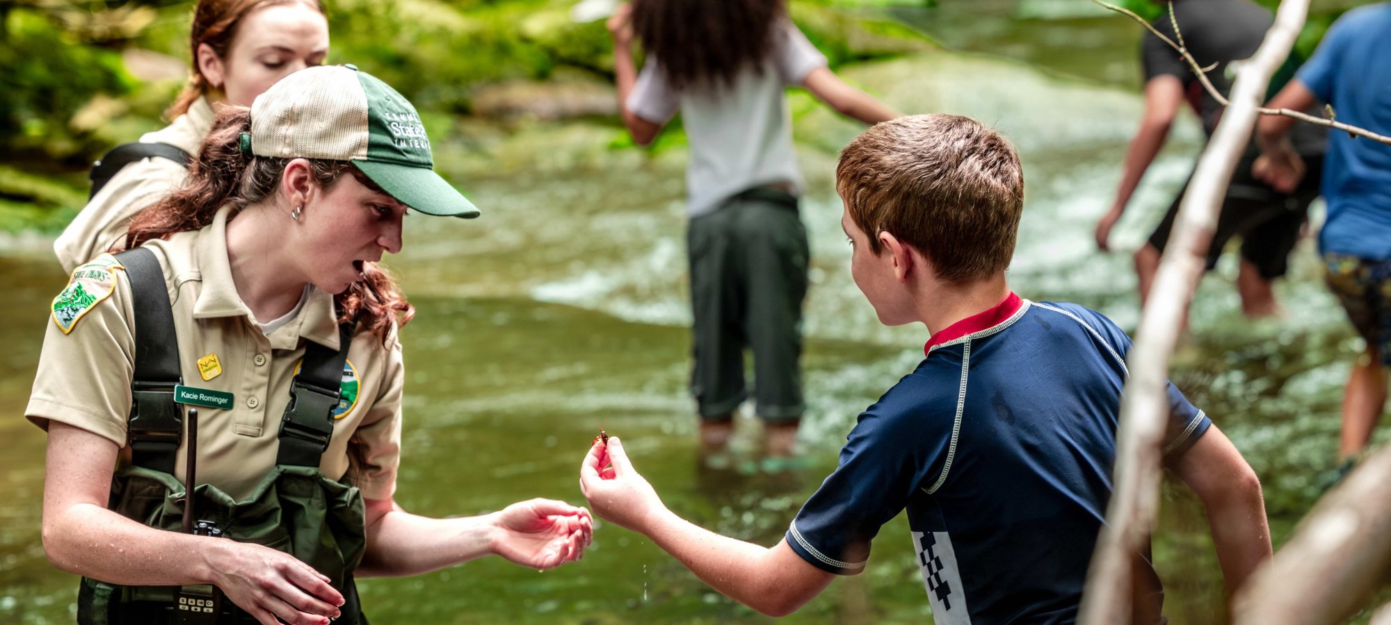 Ranger in creek looking at what child has caught in his hand