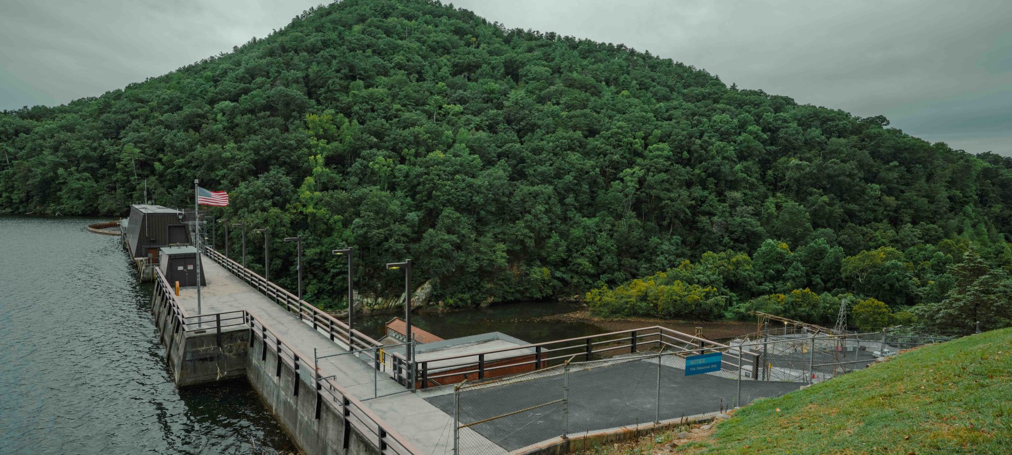 view of dam from on top of a hill and a mountain covered in trees in the distance