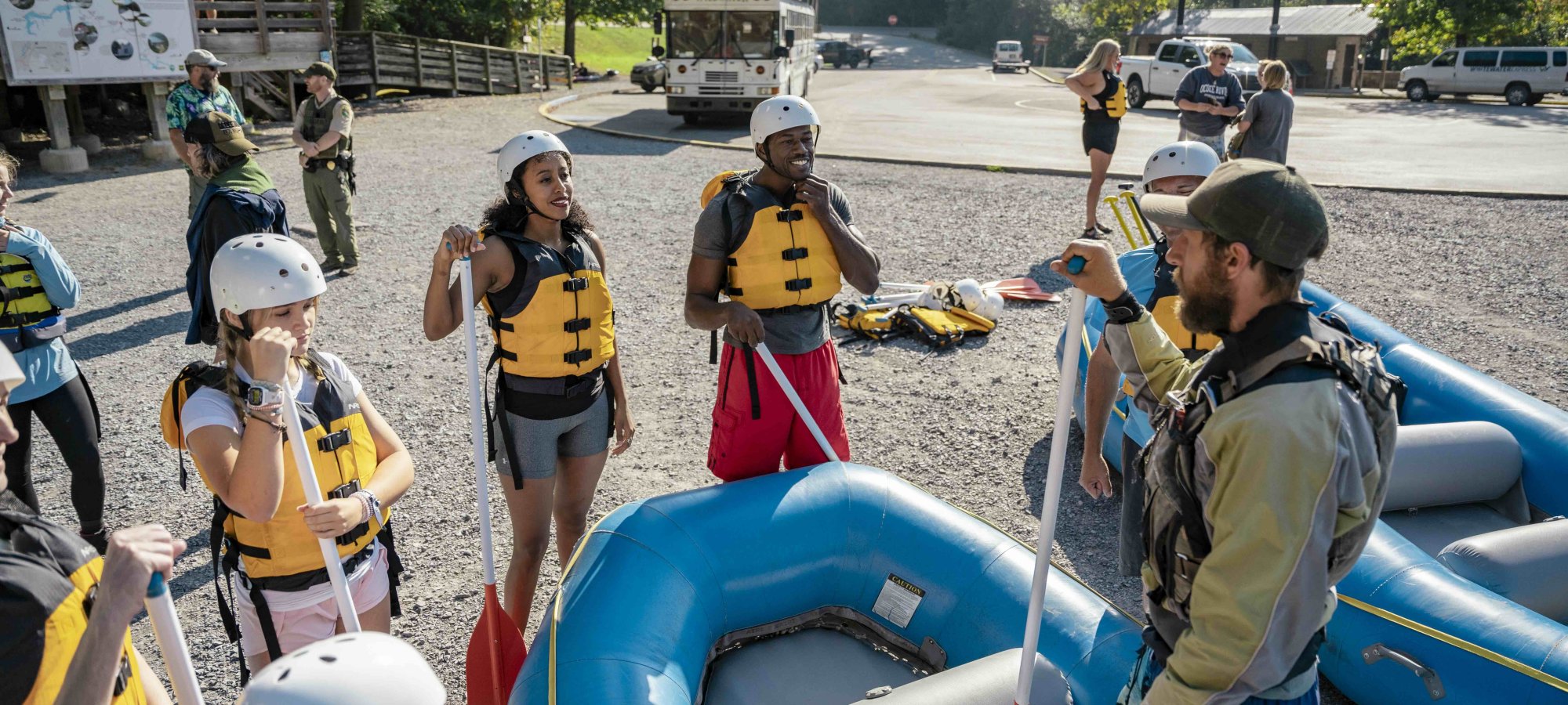 group of people wearing helmets and life vest listening to a ranger instructor on a raft