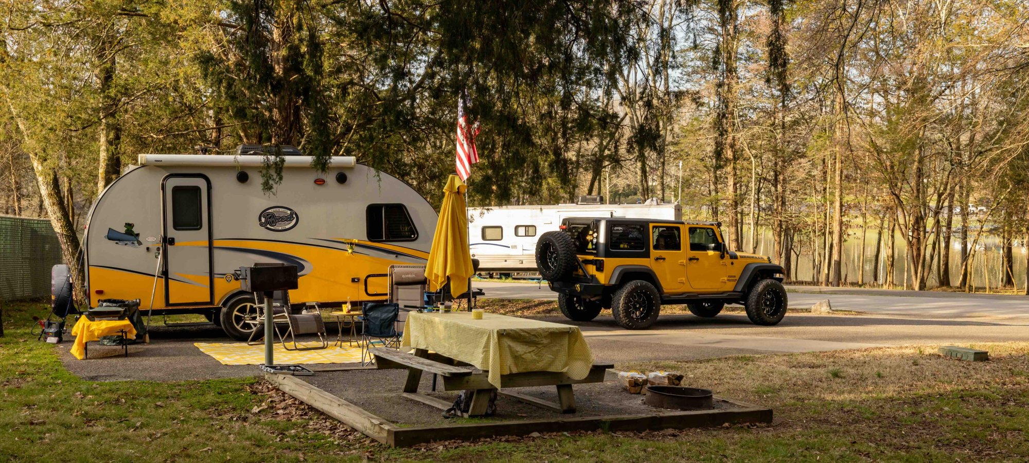 Yellow camper trailer and SUV parked at a forest campsite.