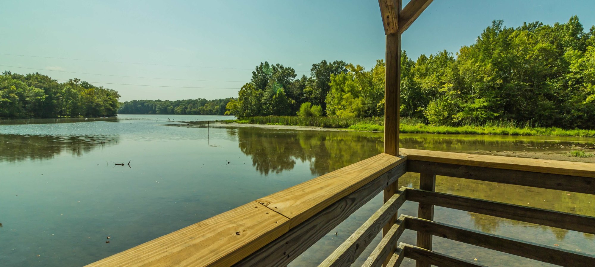 Wooden gazebo overlooking a tranquil lake surrounded by lush greenery.