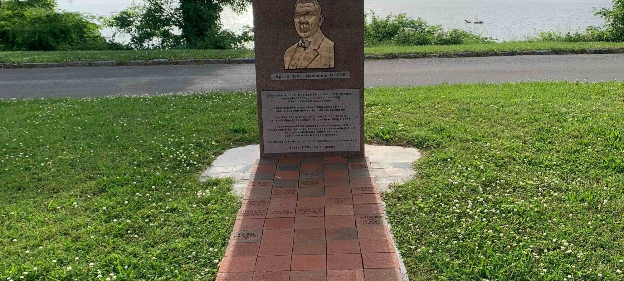 Brick pathway leading to a commemorative plaque by a lake.