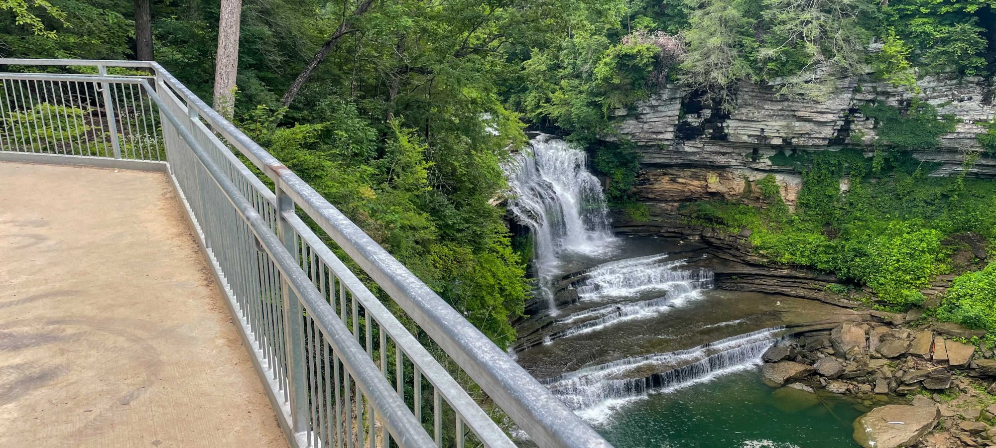 View from a bridge over a forested area with a waterfall and river.
