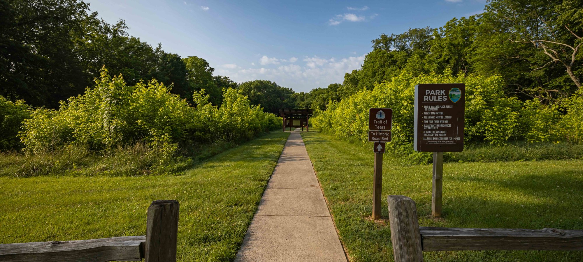 Concrete path leading into lush green park with informational signs.