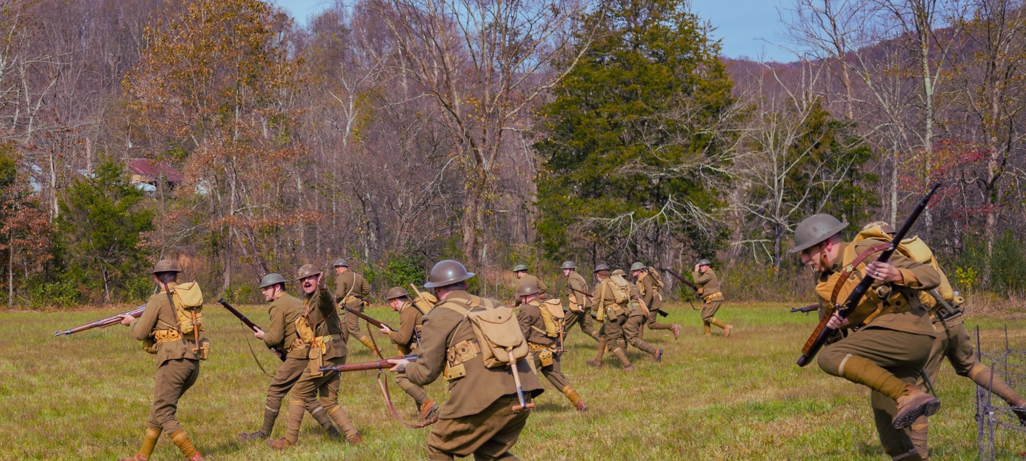 Historical reenactment of soldiers charging in a grassy field with rifles.