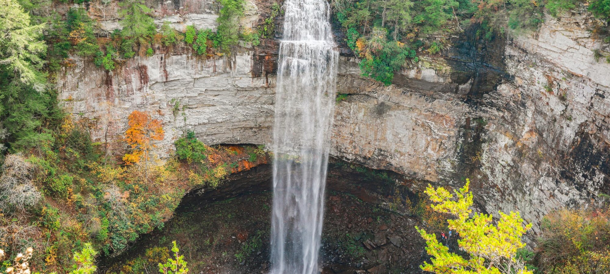 Aerial view of a tall waterfall cascading into a wooded pool.