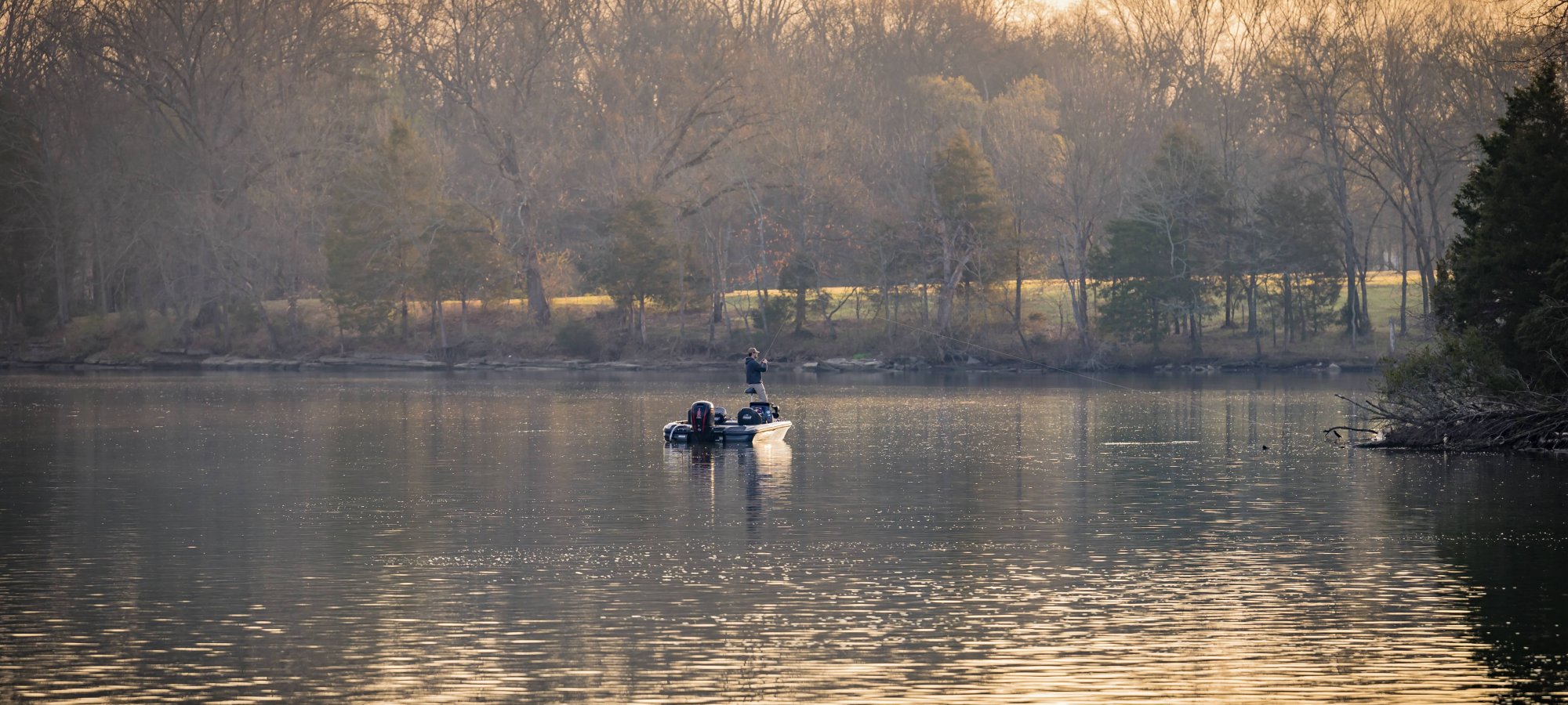 Two people rowing a boat on a tranquil lake at sunset.