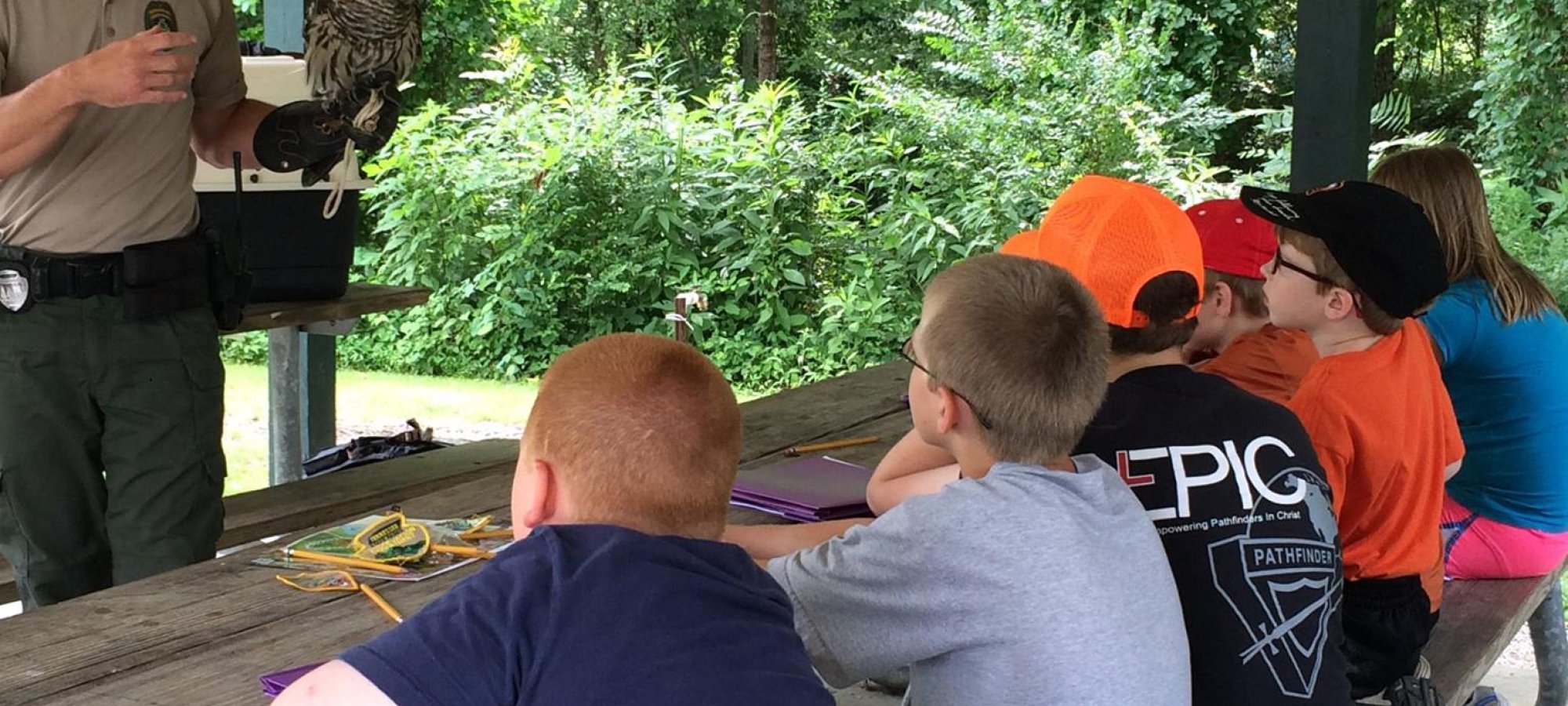 Ranger showing turtle to attentive children at outdoor park pavilion.